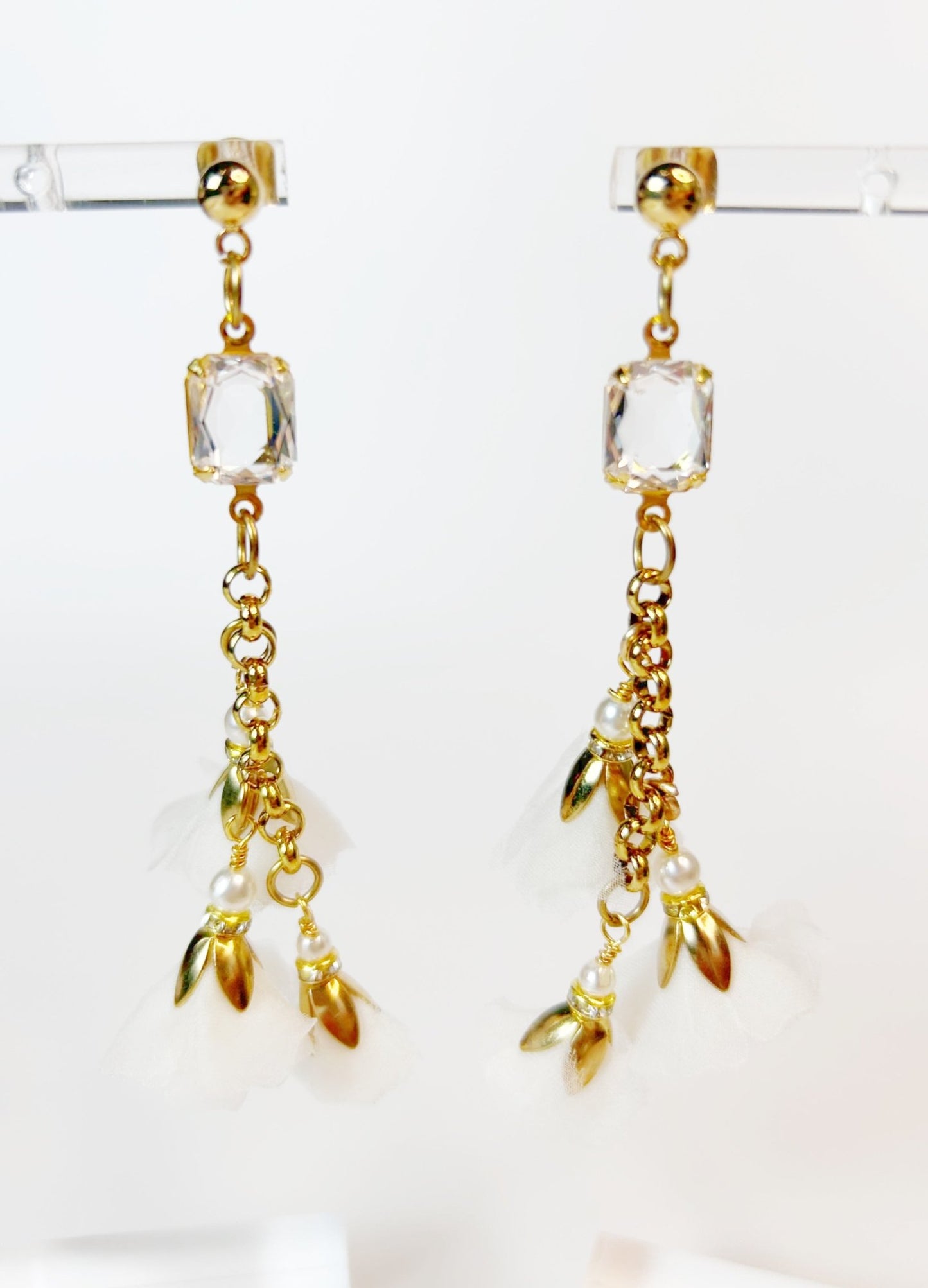 Gold earrings with clear crystals and leaf-like charms on a white background