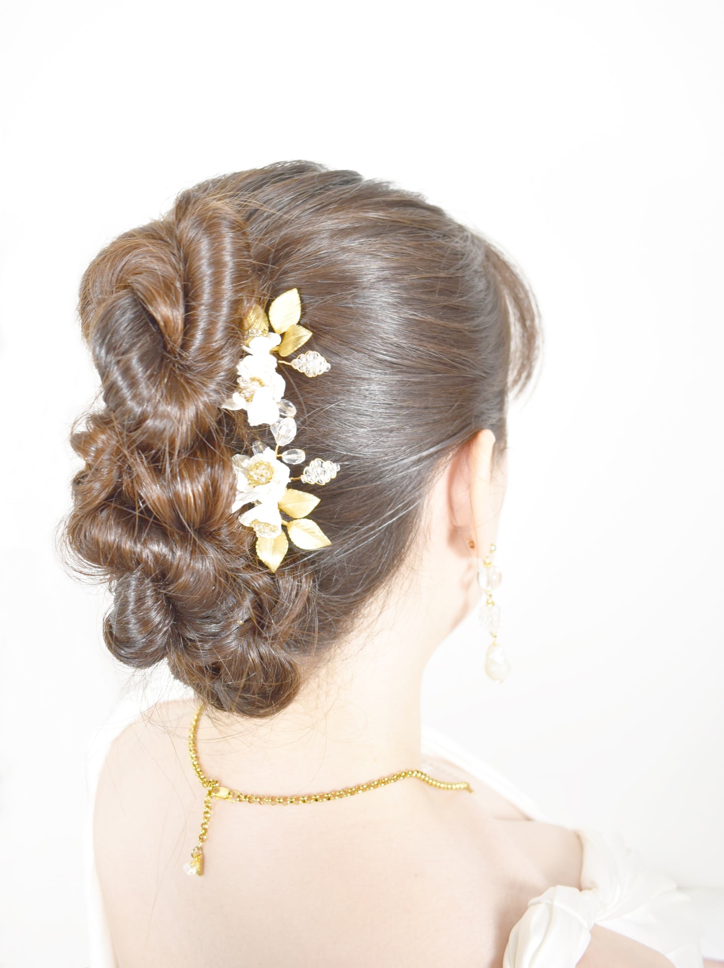 Woman with styled hair featuring gold floral hairpiece on a white background