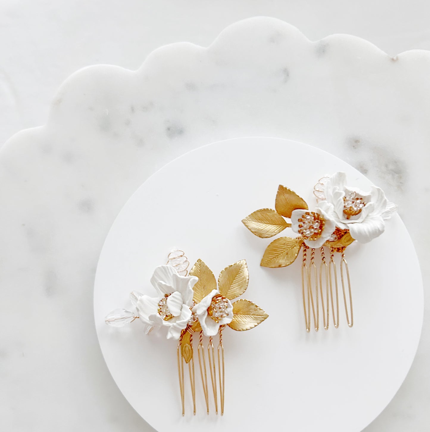 Gold and white floral hair combs on a white plate with a marble background