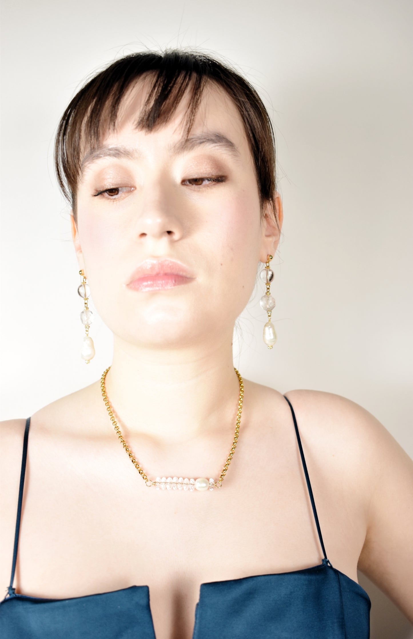 Woman wearing a blue dress and gold necklace with a plain background