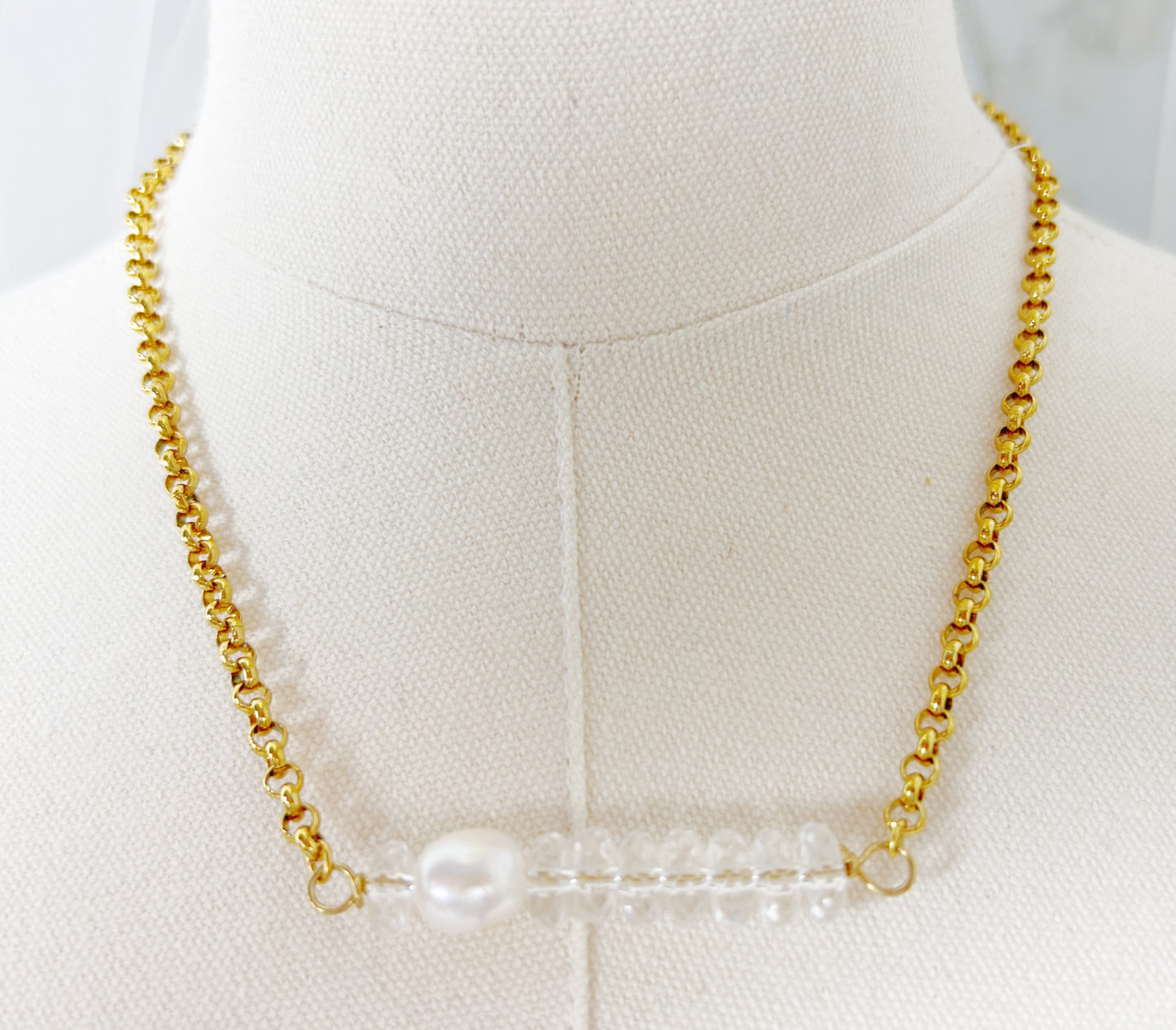 Gold chain necklace with a central pearl on a mannequin bust.