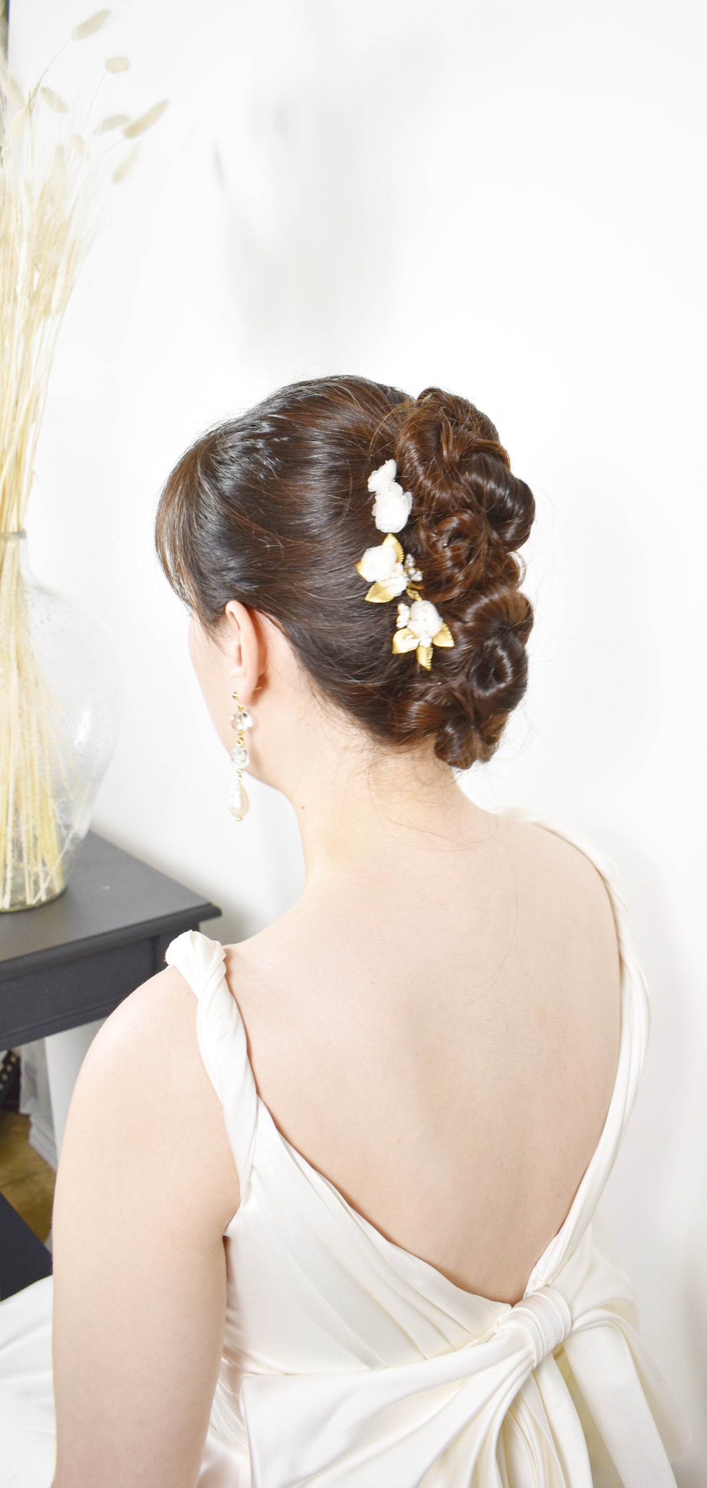Woman with elegant hair styled in an updo with floral accessories, wearing a white dress.