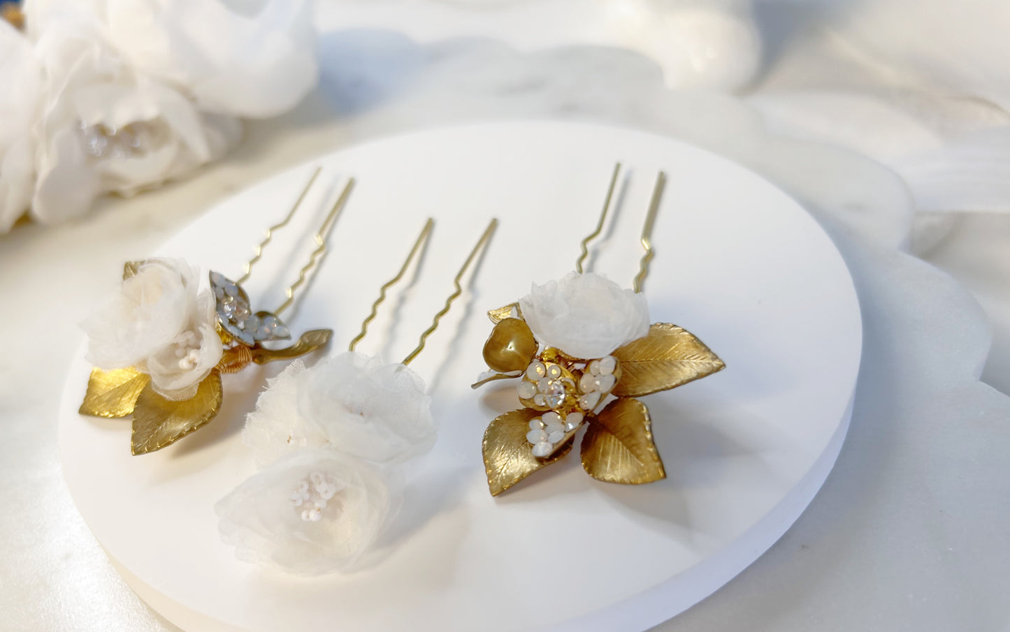 Decorative hair pins with gold and white flowers on a white surface