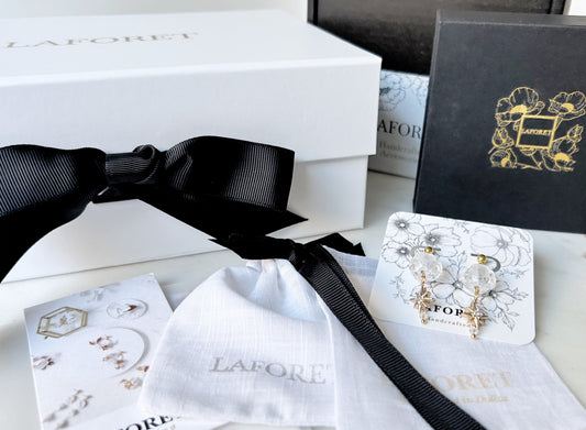 LAFORET signature packaging suite featuring white soft-touch boxes with gold stamping, black gift boxes with floral gold foil, linen pouches, black grosgrain ribbon, and branded printed cards.