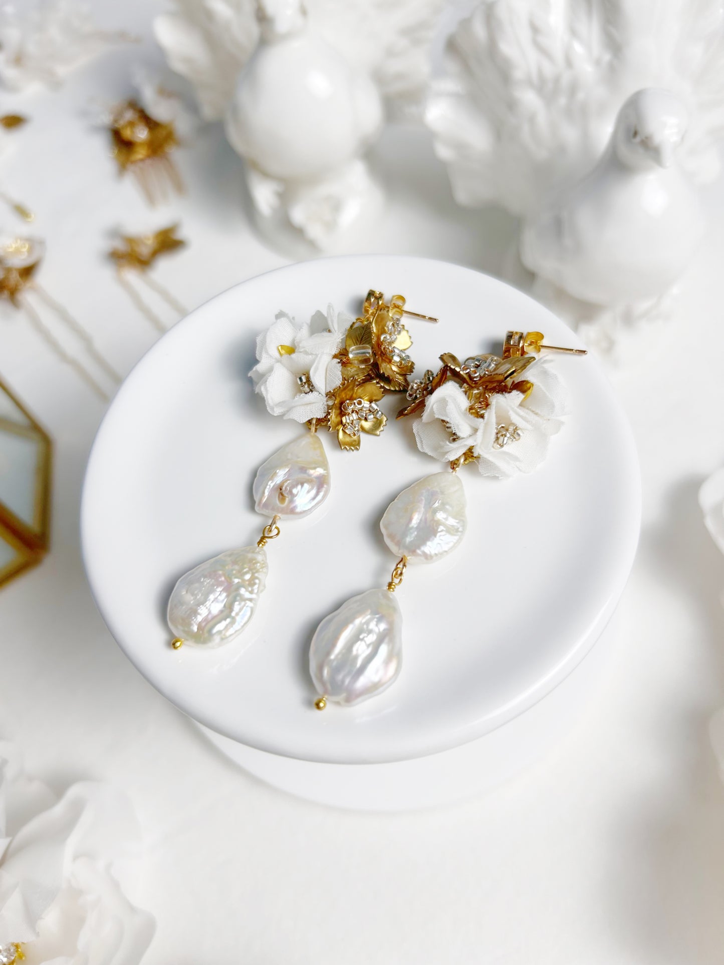 Pearl and gold earrings on a white dish with a white background