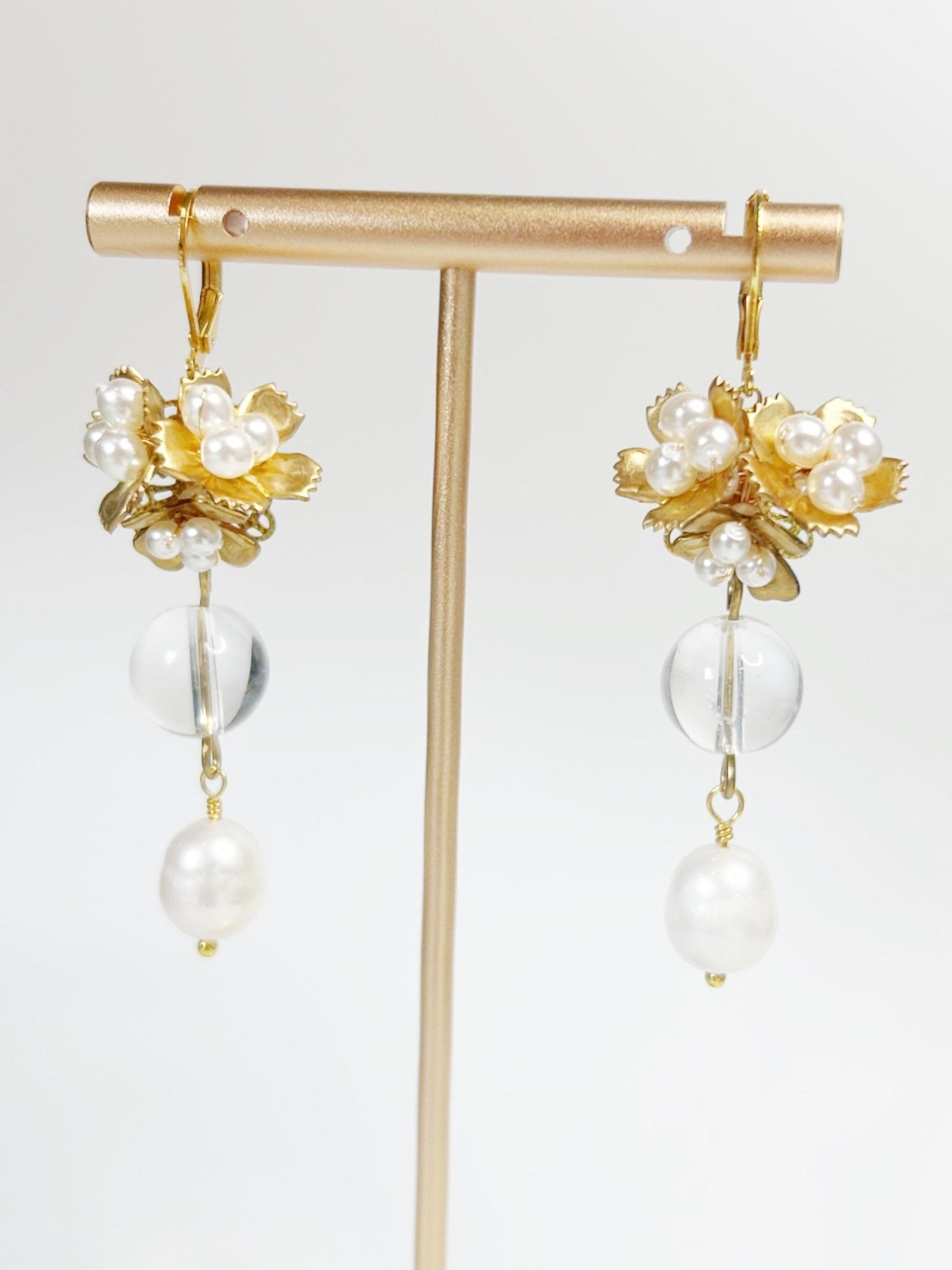 Gold and pearl earrings on a gold stand against a white background