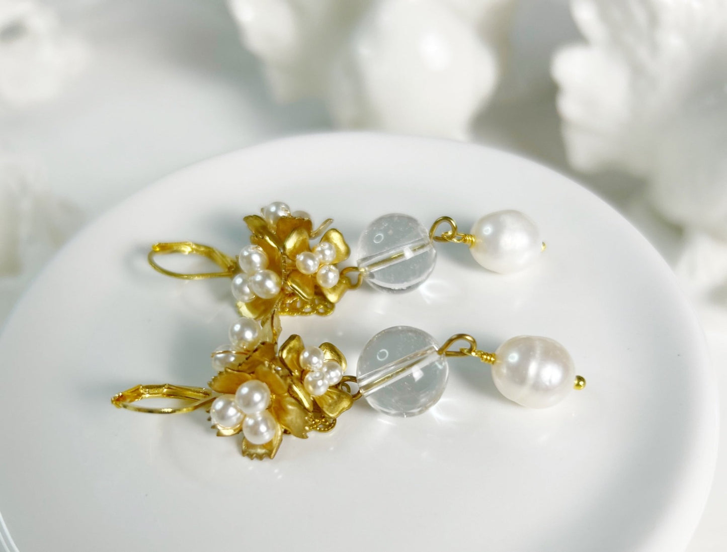 Gold and pearl earrings on a white surface with a blurred background