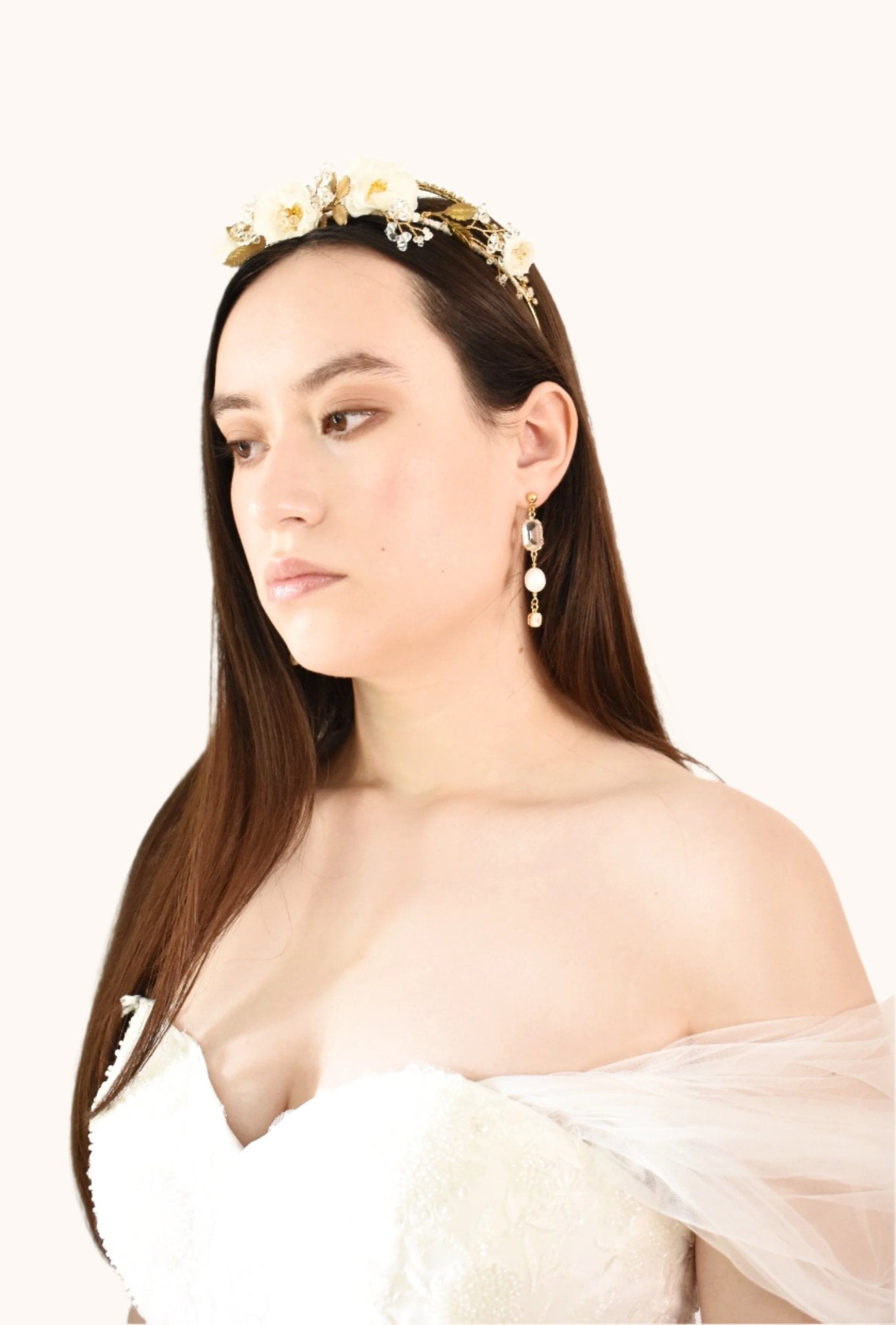 Woman wearing a gold headband and pearl earrings against a plain background