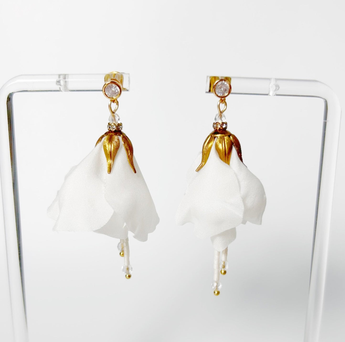 Pair of white floral earrings with gold accents on a clear stand.