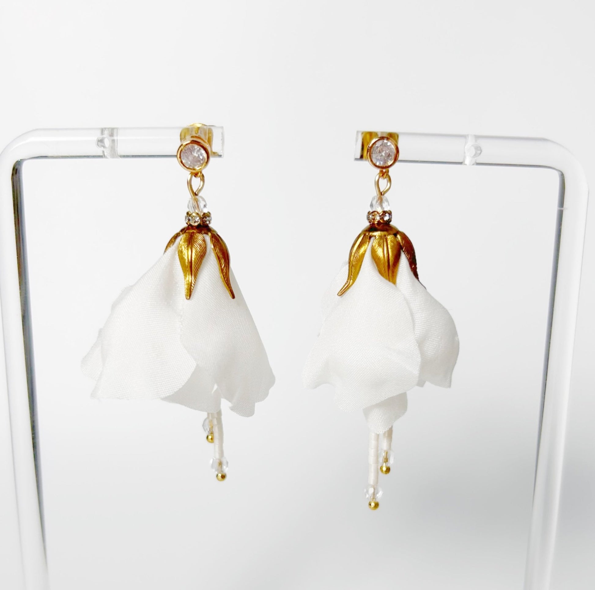 Pair of white floral earrings with gold accents on a clear stand.