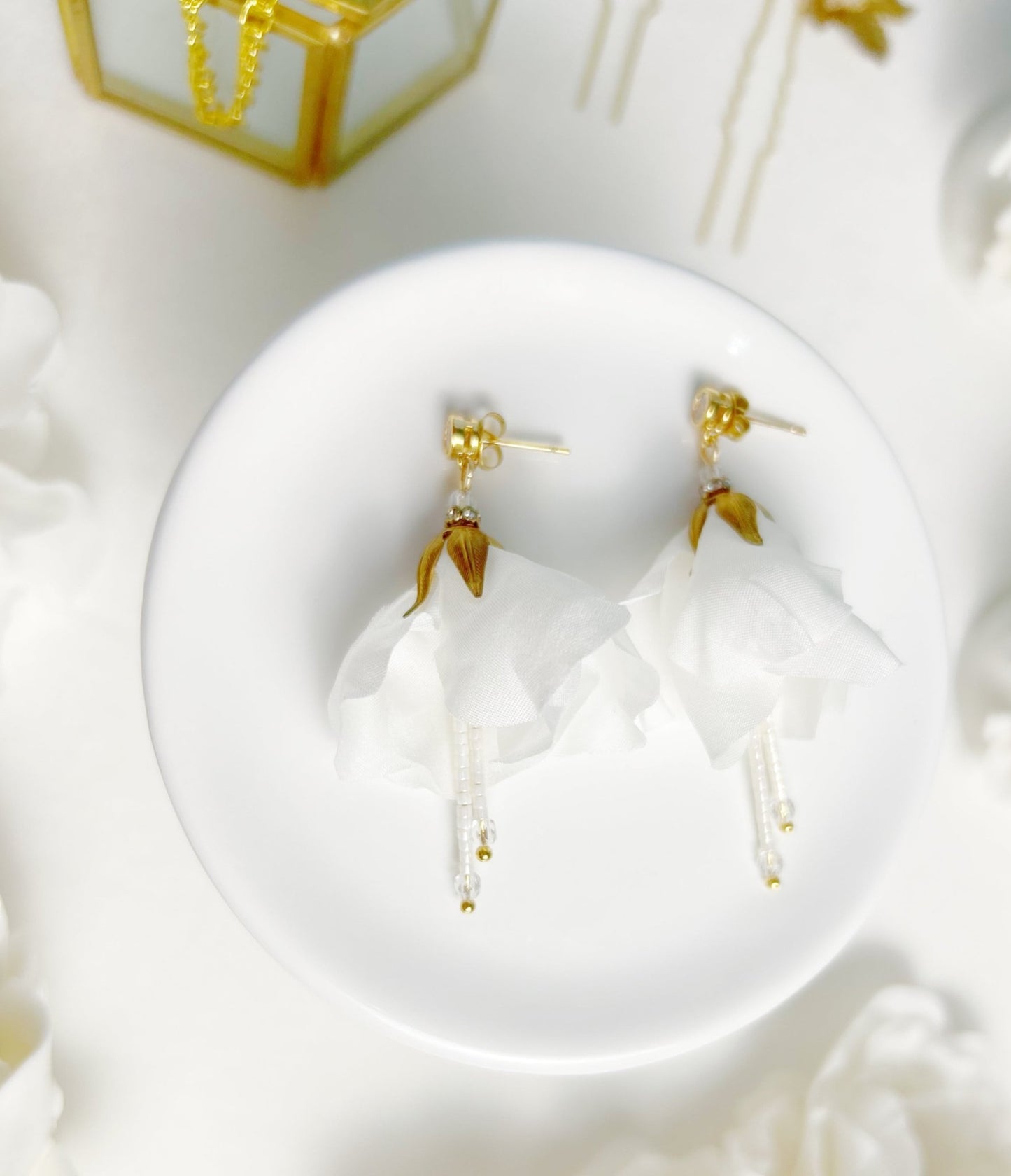 Gold earrings on a white dish with a decorative background