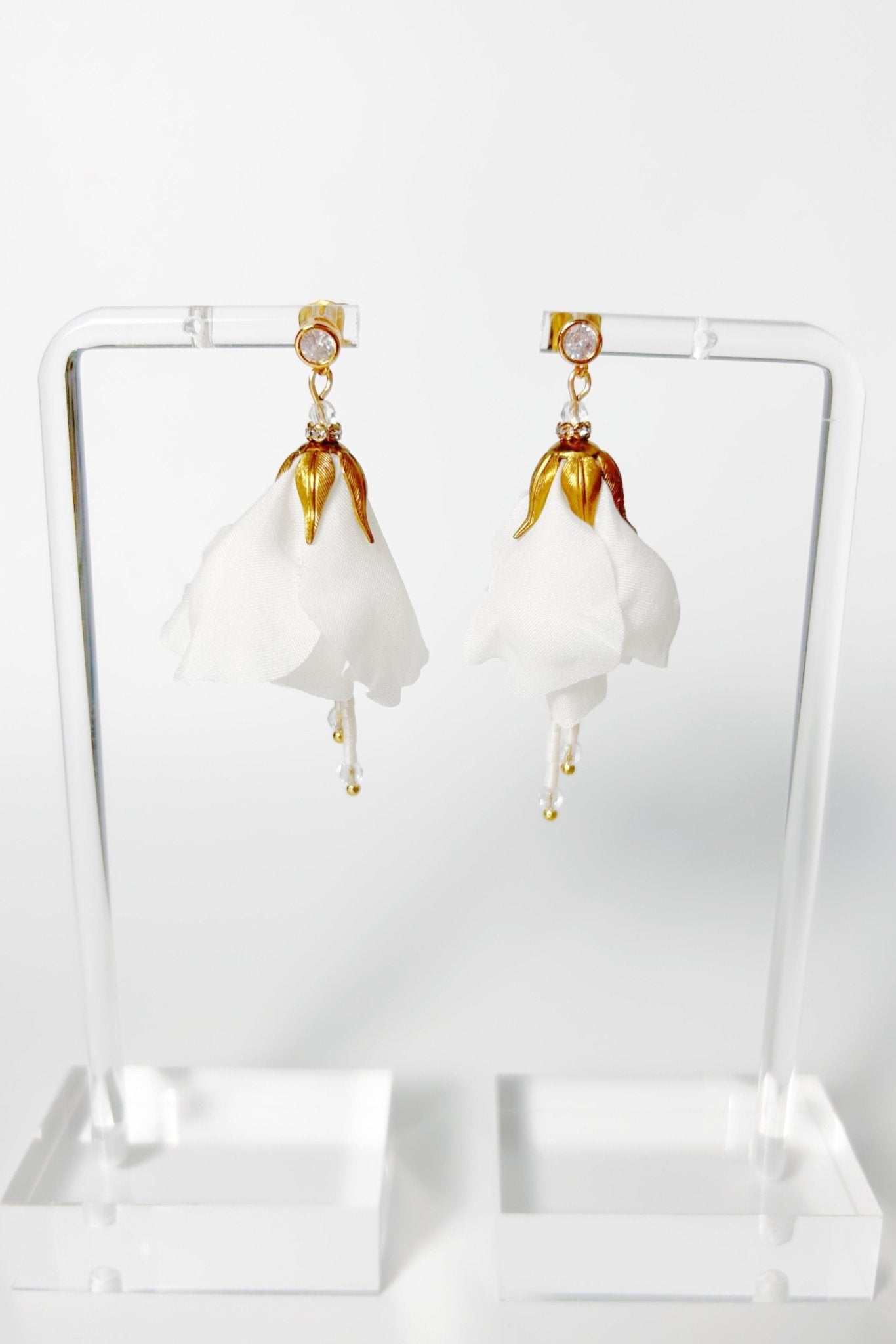 Pair of white earrings with gold accents on a clear stand against a white background