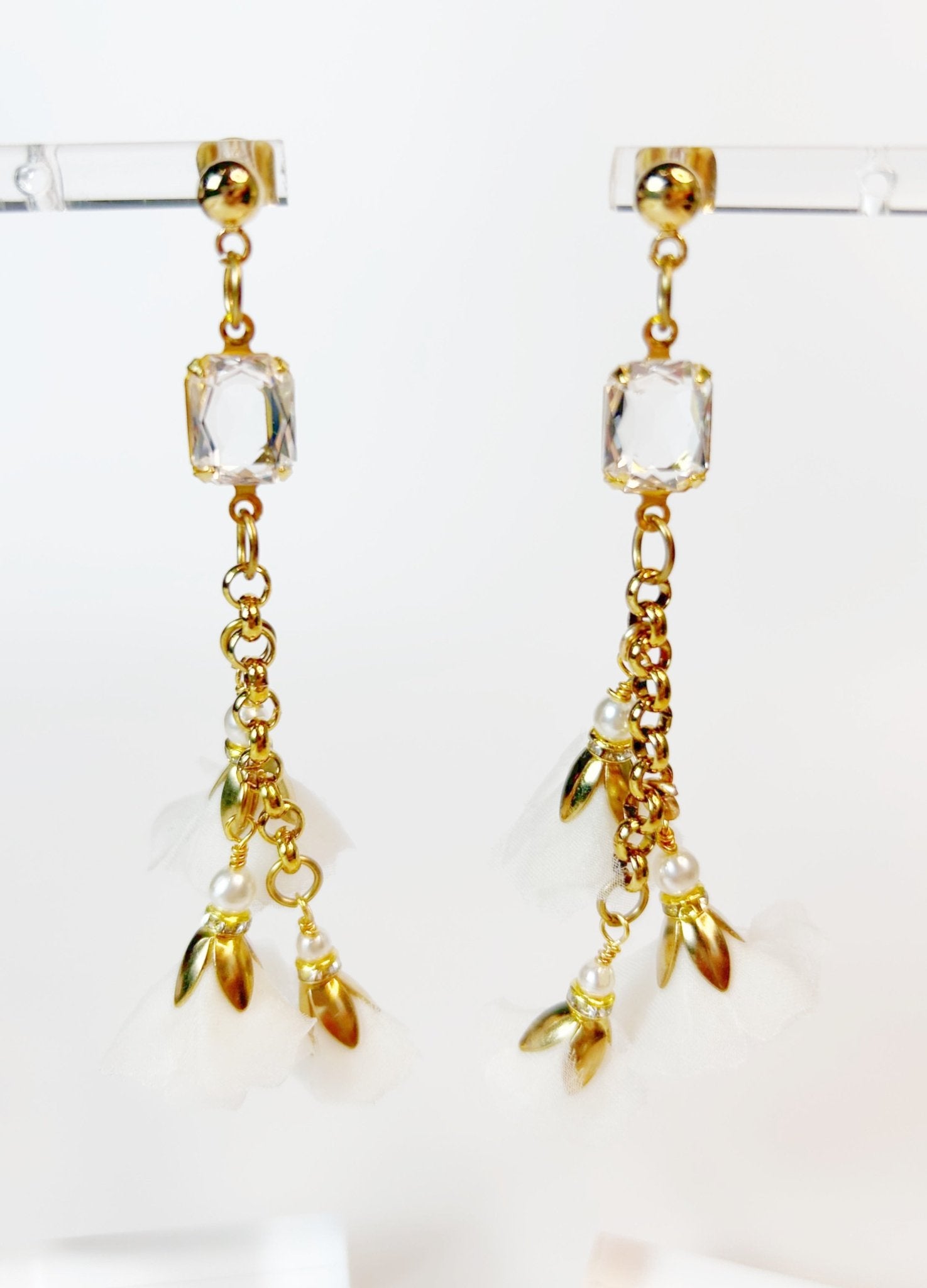 Gold earrings with clear crystals and leaf-like charms on a white background
