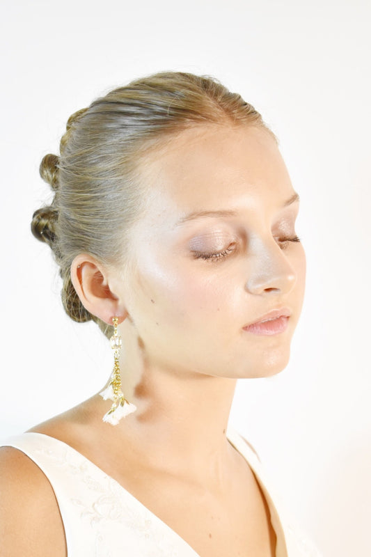 Woman with styled hair, flower earrings and makeup on a white background