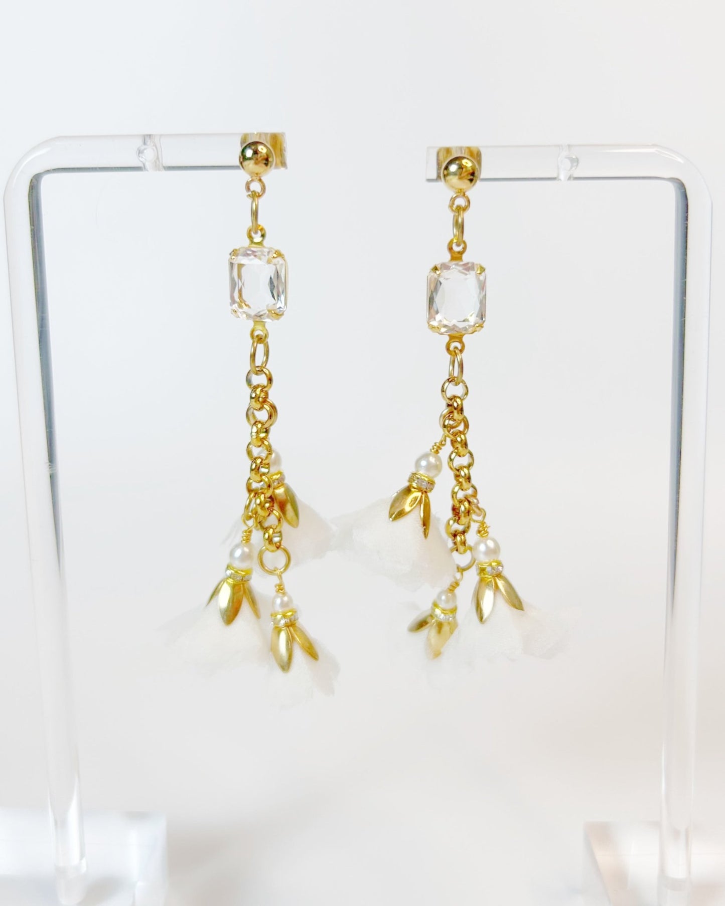 Gold earrings with crystal and pearl-like charms on a clear stand.
