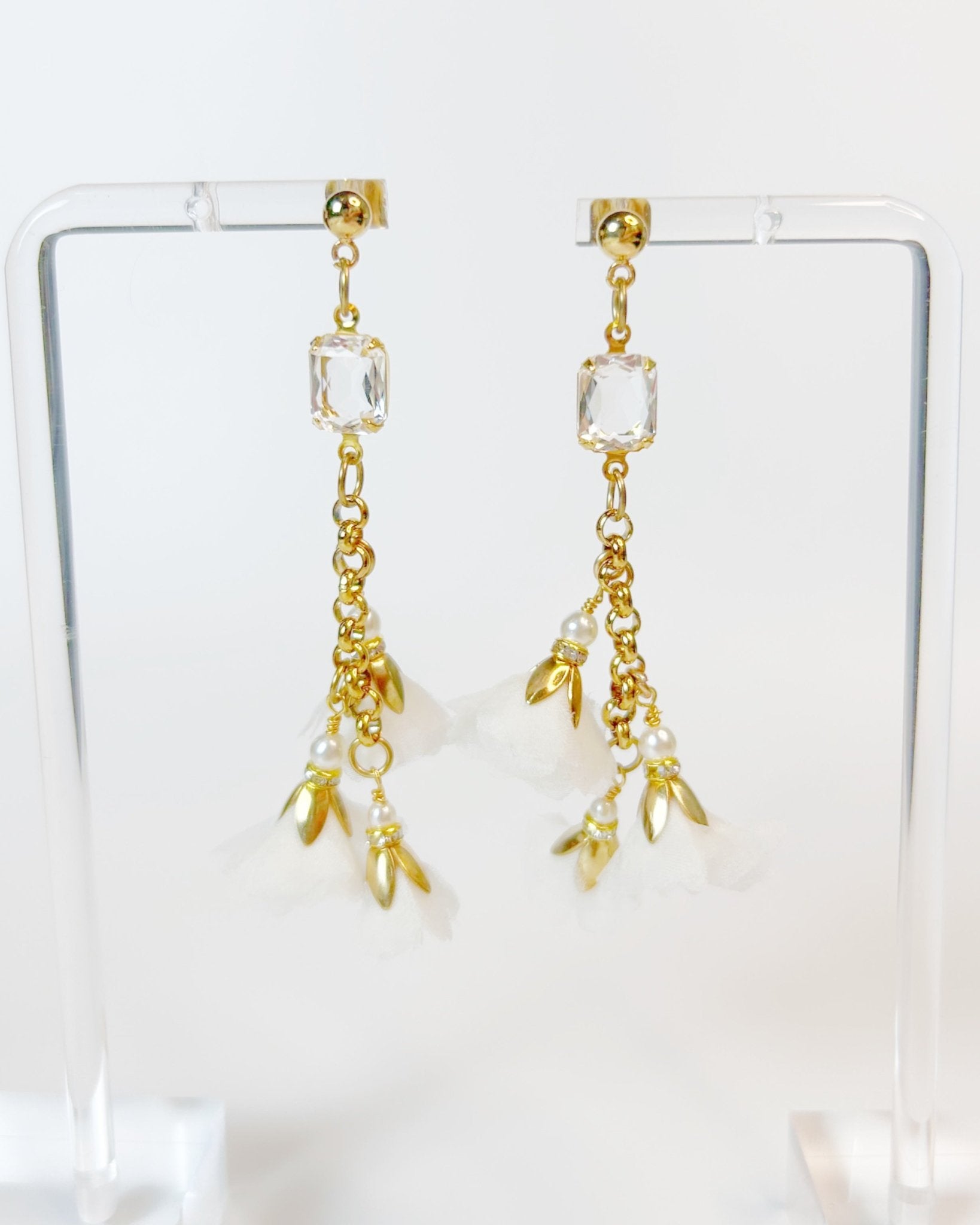 Gold earrings with crystal and pearl-like charms on a clear stand.