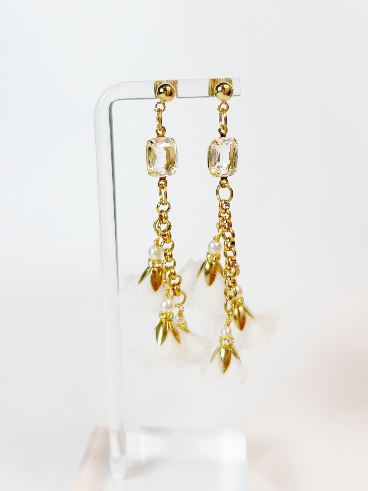 Gold earrings with clear gemstones and pearl-like elements on a white background