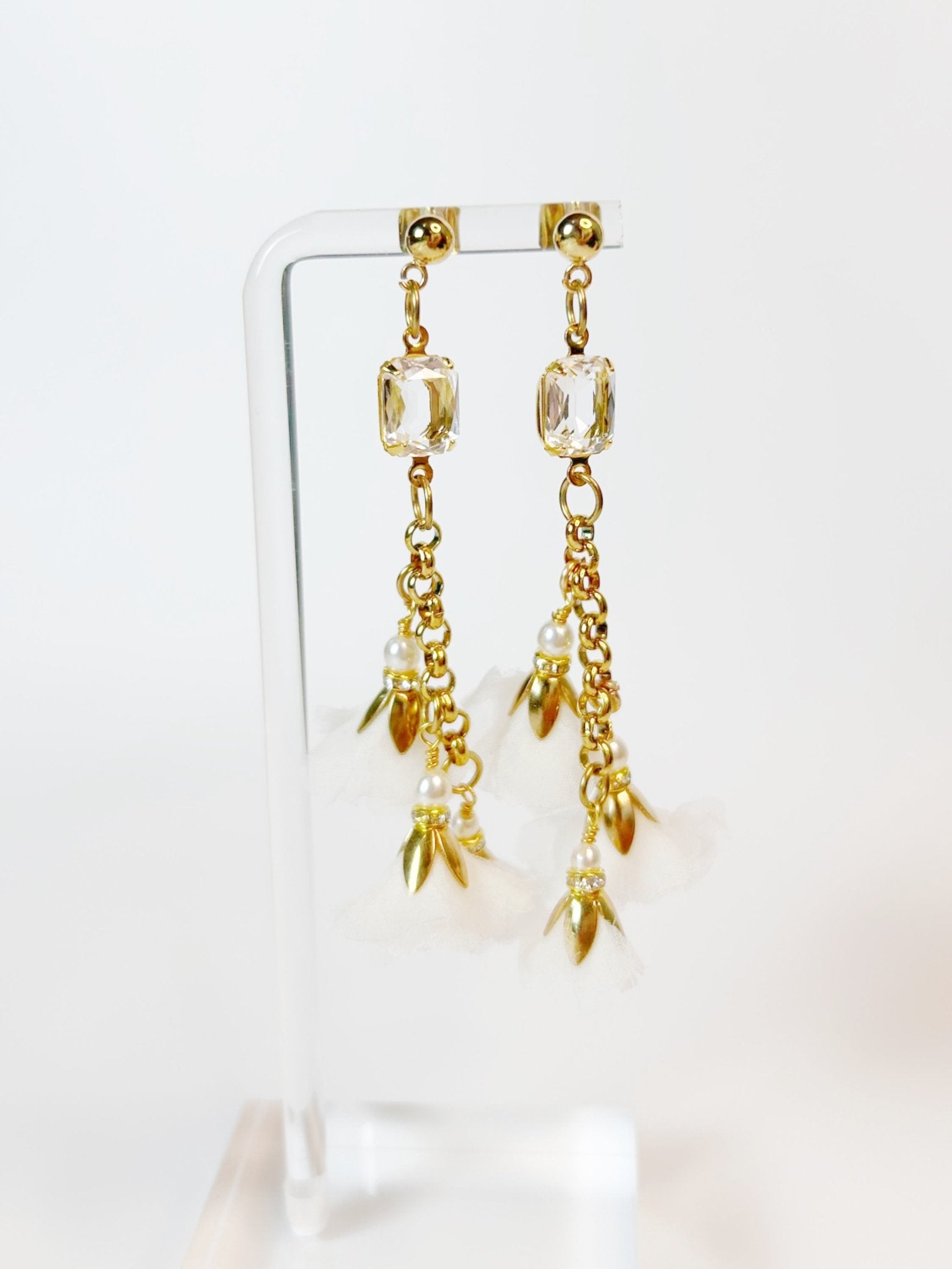 Gold earrings with clear gemstones and pearl-like elements on a white background