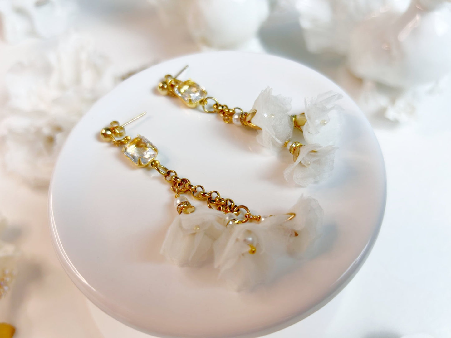 Gold and white earrings on a white shell with a blurred natural background