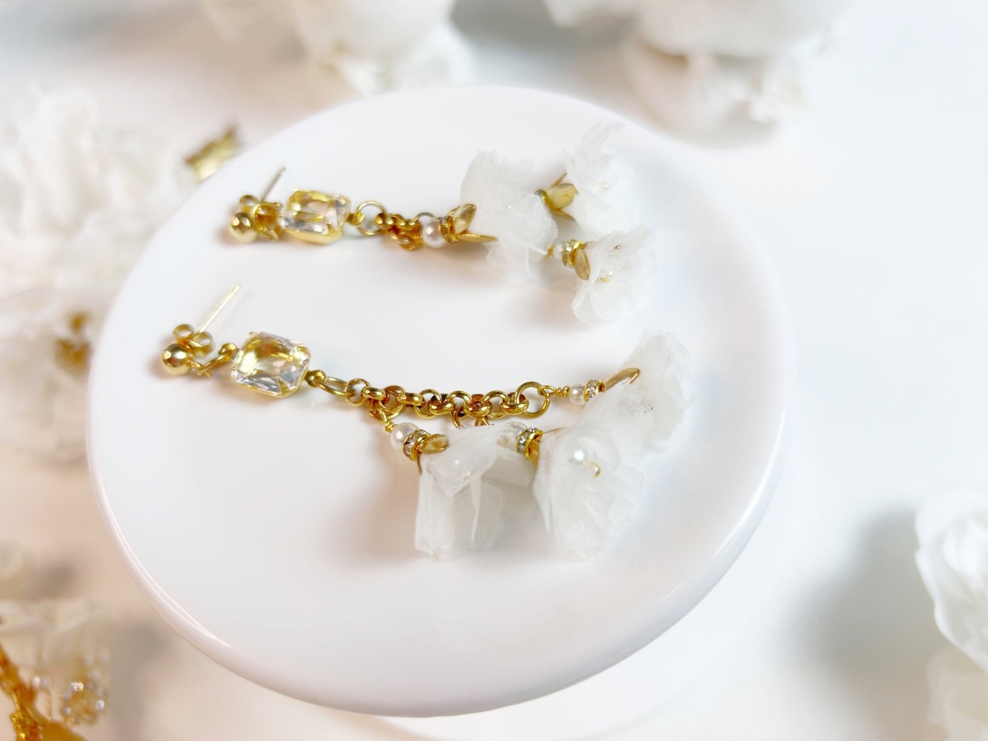 Gold and crystal earrings on a white dish with a soft focus background