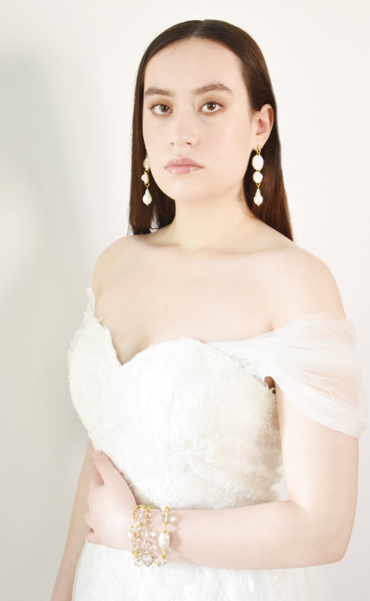 Woman wearing a white off-shoulder top with long earrings against a plain background