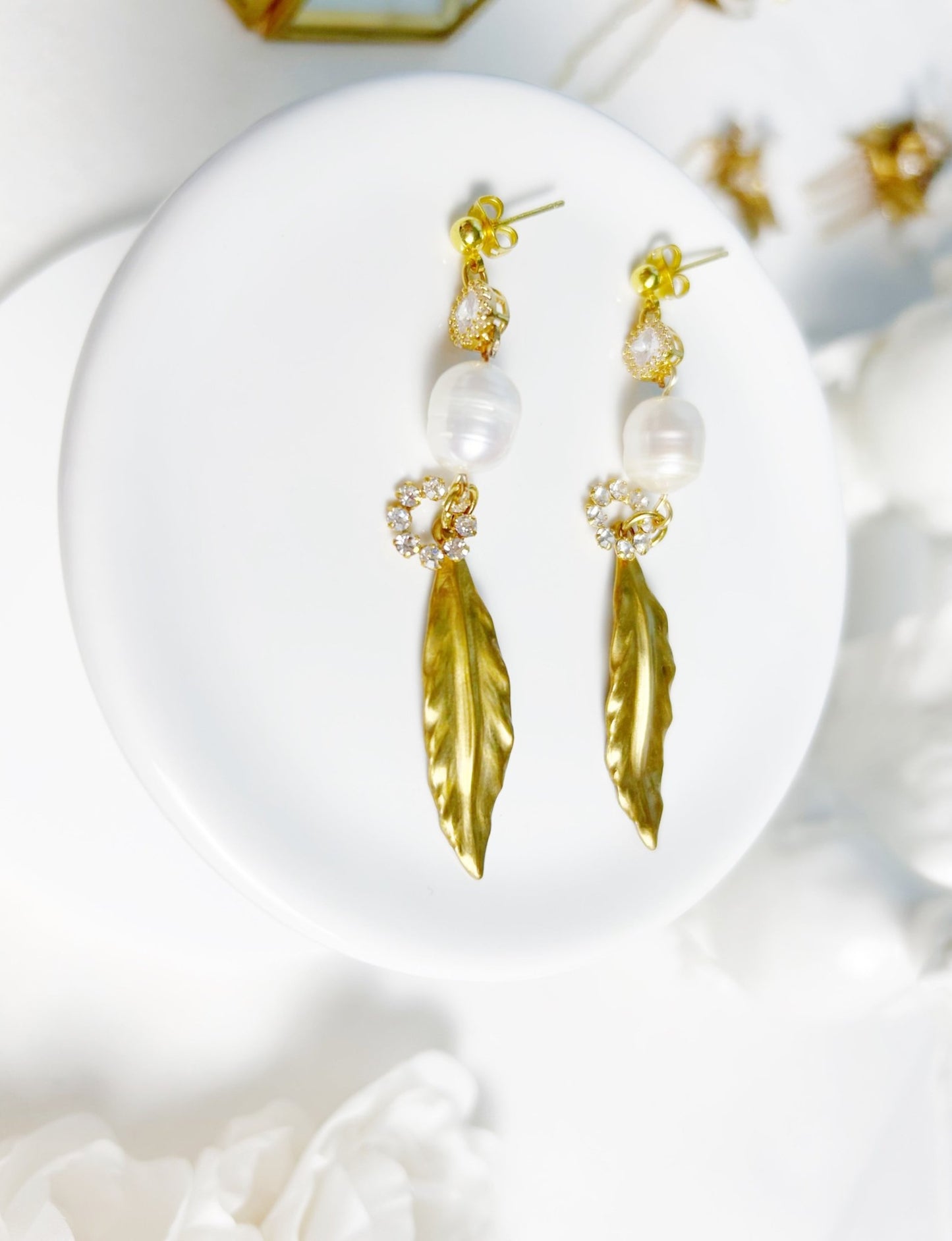 Gold feather earrings with pearl-like beads on a white surface