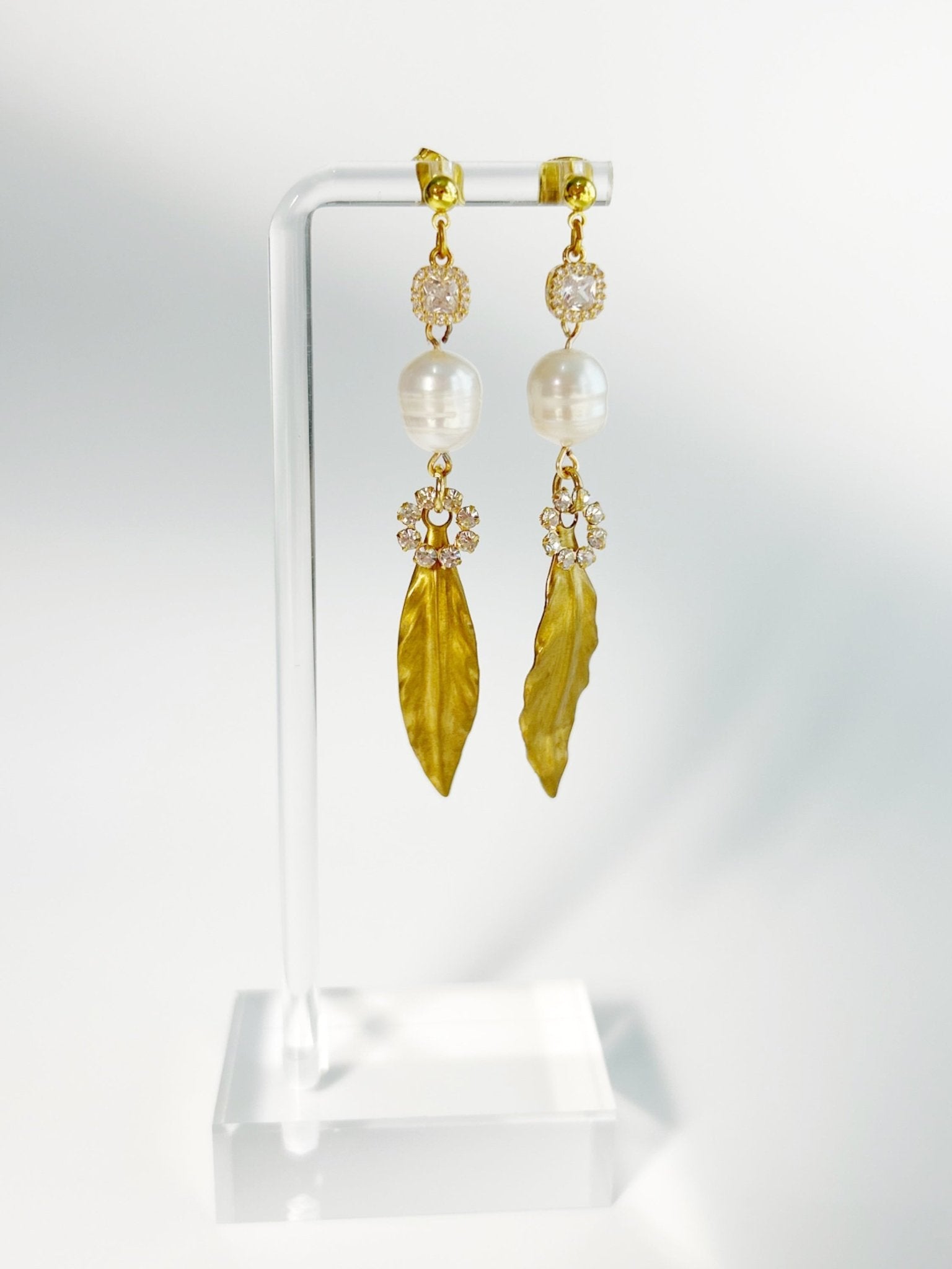 Gold leaf earrings on a clear stand with a white background