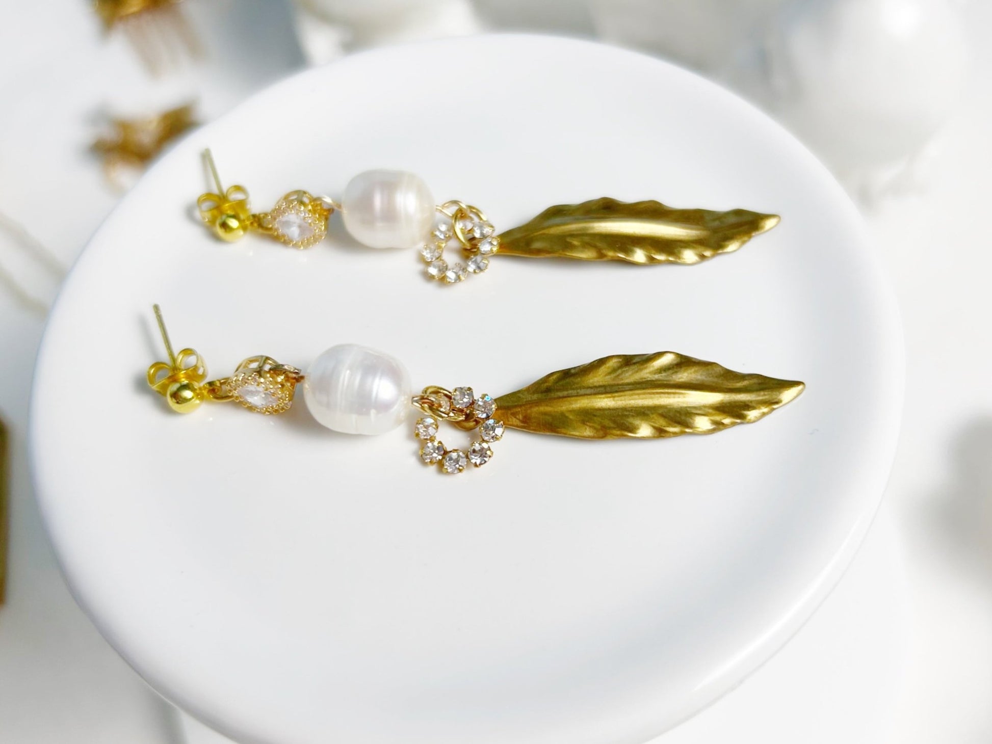 Gold leaf earrings with pearl-like beads on a white plate