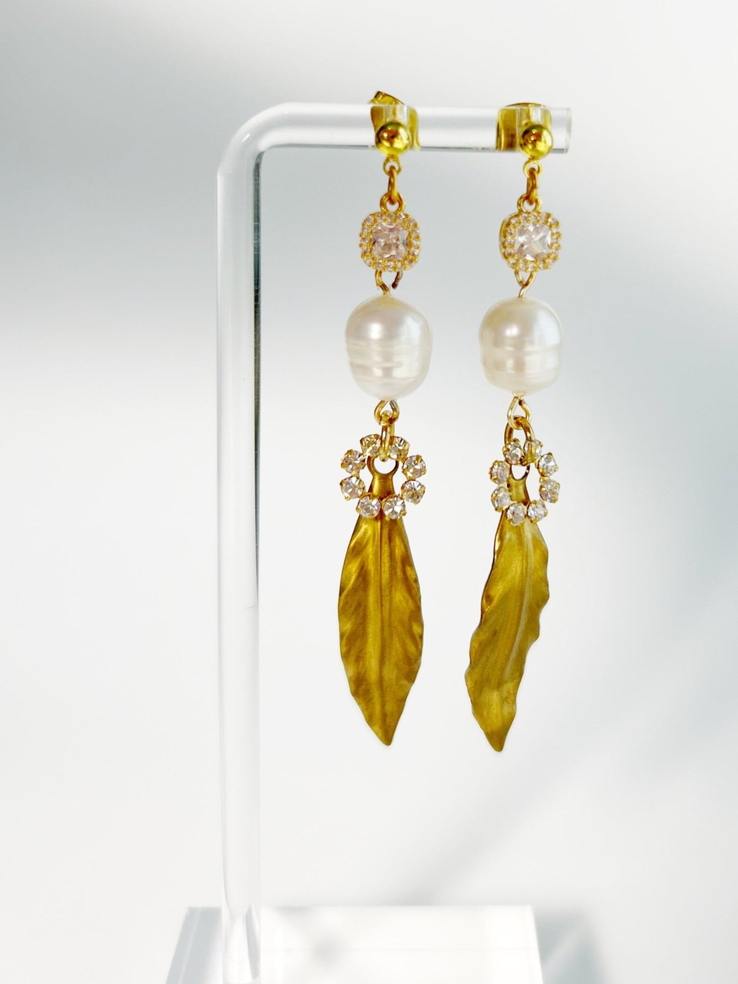 Gold earrings with pearl and leaf-like stone on a white background
