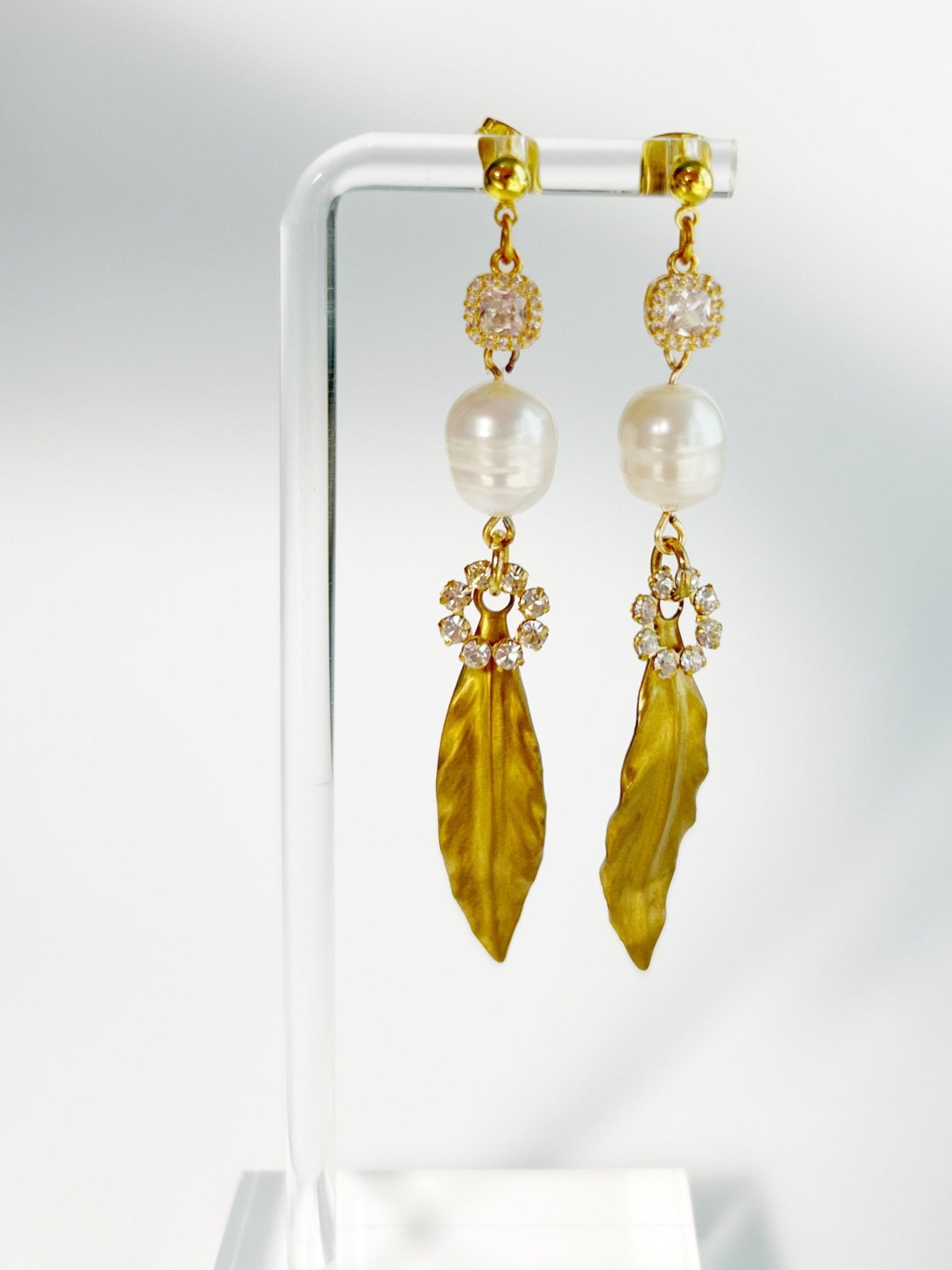 Gold earrings with pearl and leaf-like stone on a white background