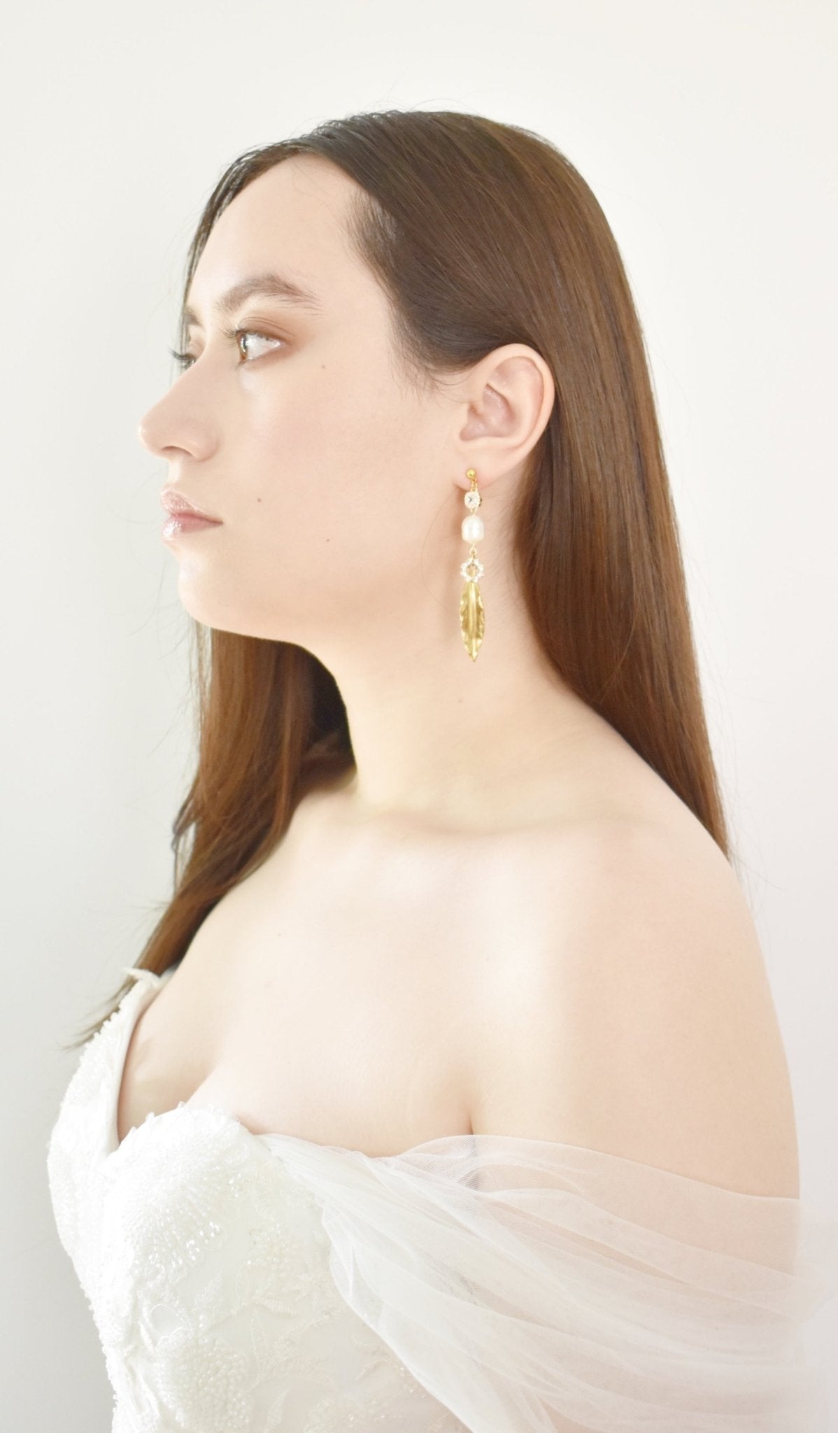 Woman wearing gold earrings with pearls against a white background