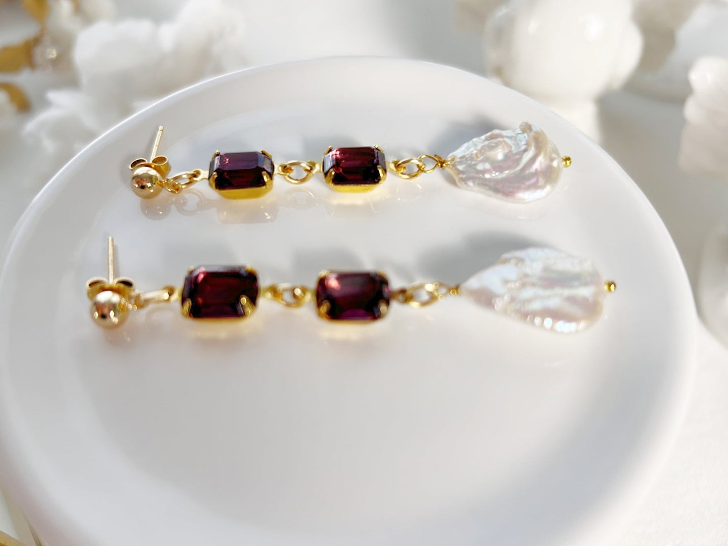 Pair of gold earrings with red and clear gemstones on a white surface.
