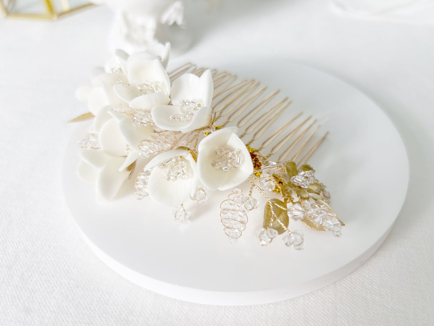 Bride hair comb with white flowers and gold accents on a white plate