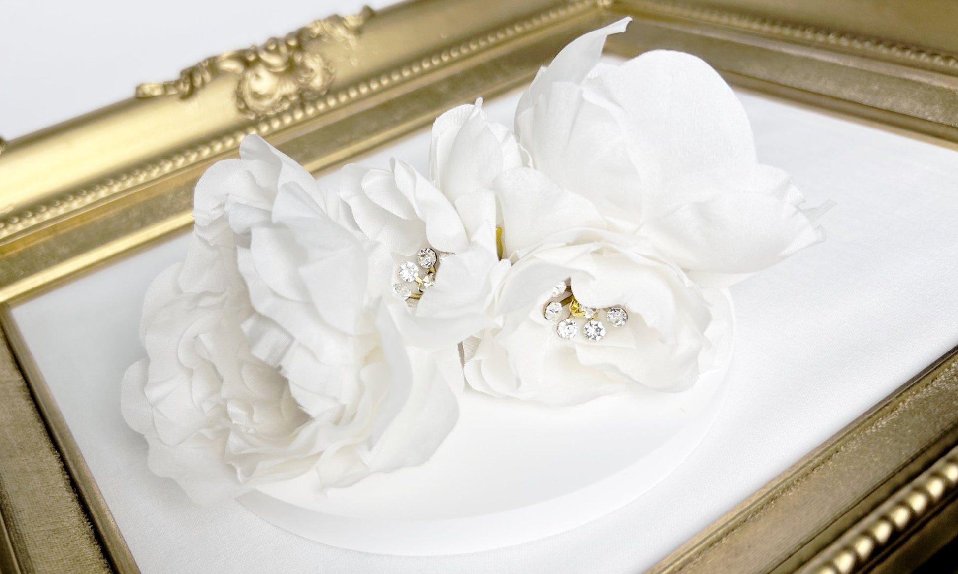 White floral hair accessories with gold centers on a white surface with a gold frame.