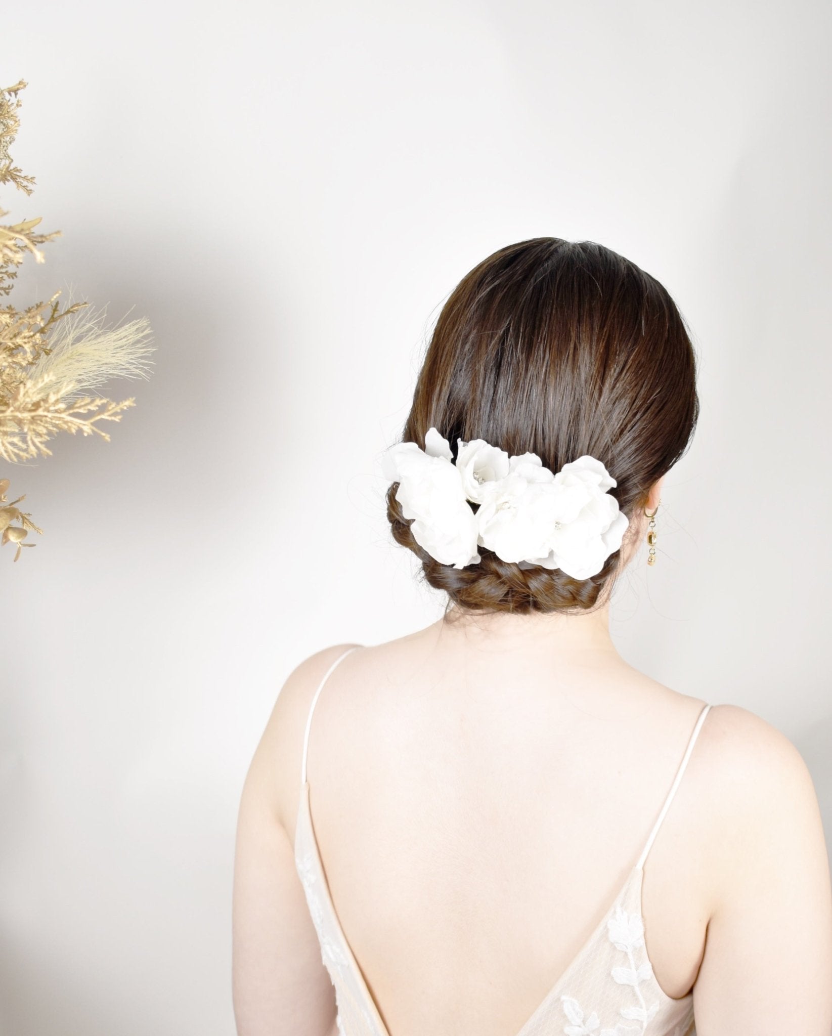 Woman with a stylish hairdo featuring white flowers against a neutral background