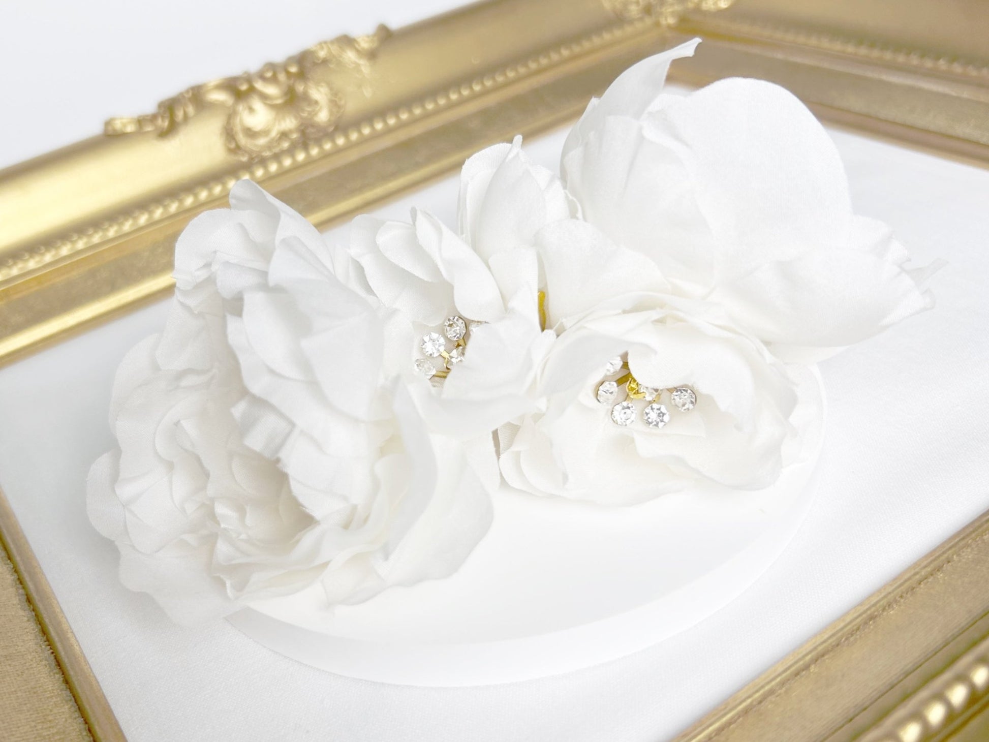 White floral earrings with pearl accents on a white surface with a gold frame.
