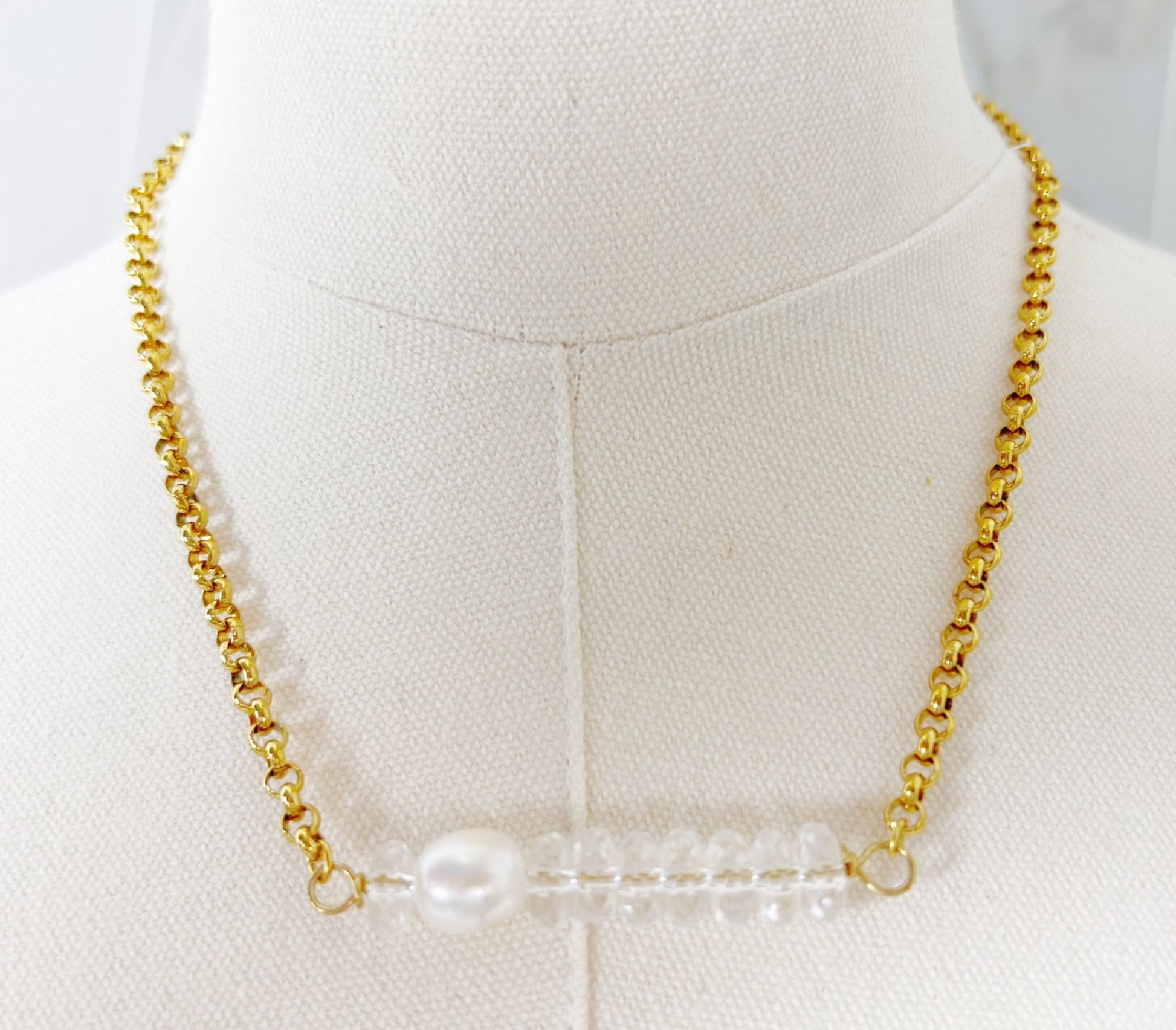 Gold chain necklace with a central pearl on a mannequin bust.