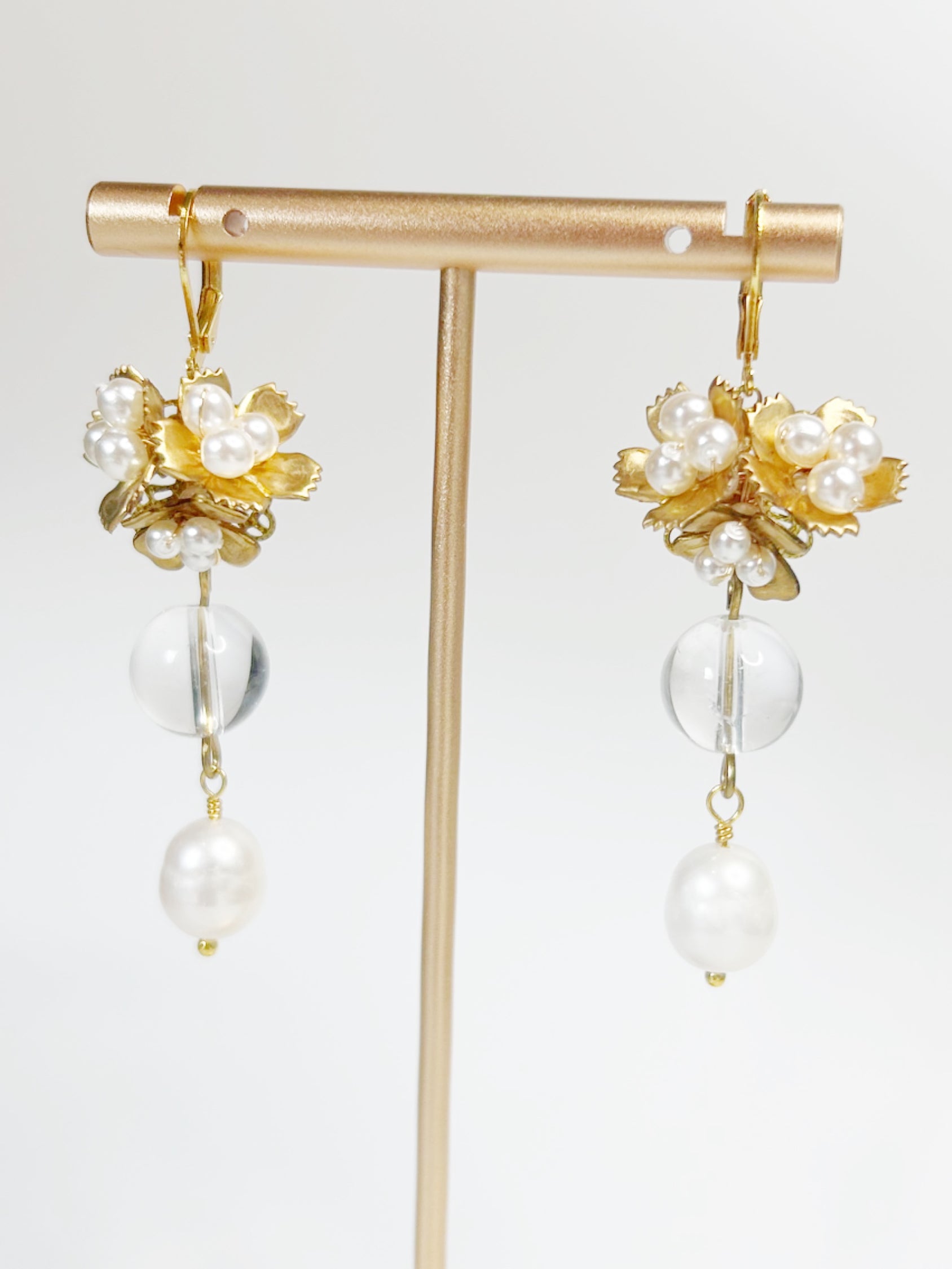 Gold and pearl earrings on a gold stand against a white background