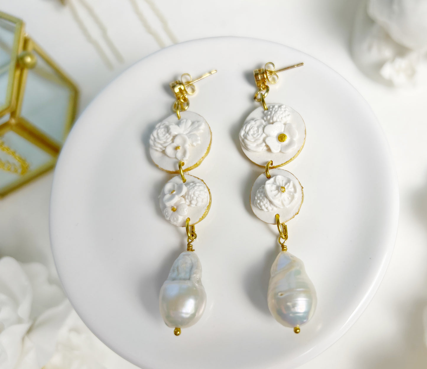 Pair of earrings with gold accents and pearl-like beads on a white plate.