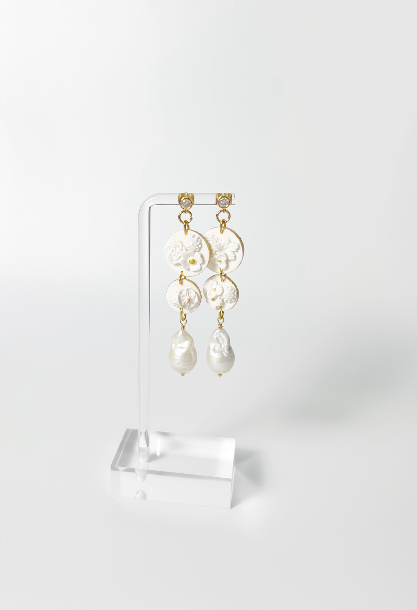 Pair of pearl earrings on a clear stand against a white background