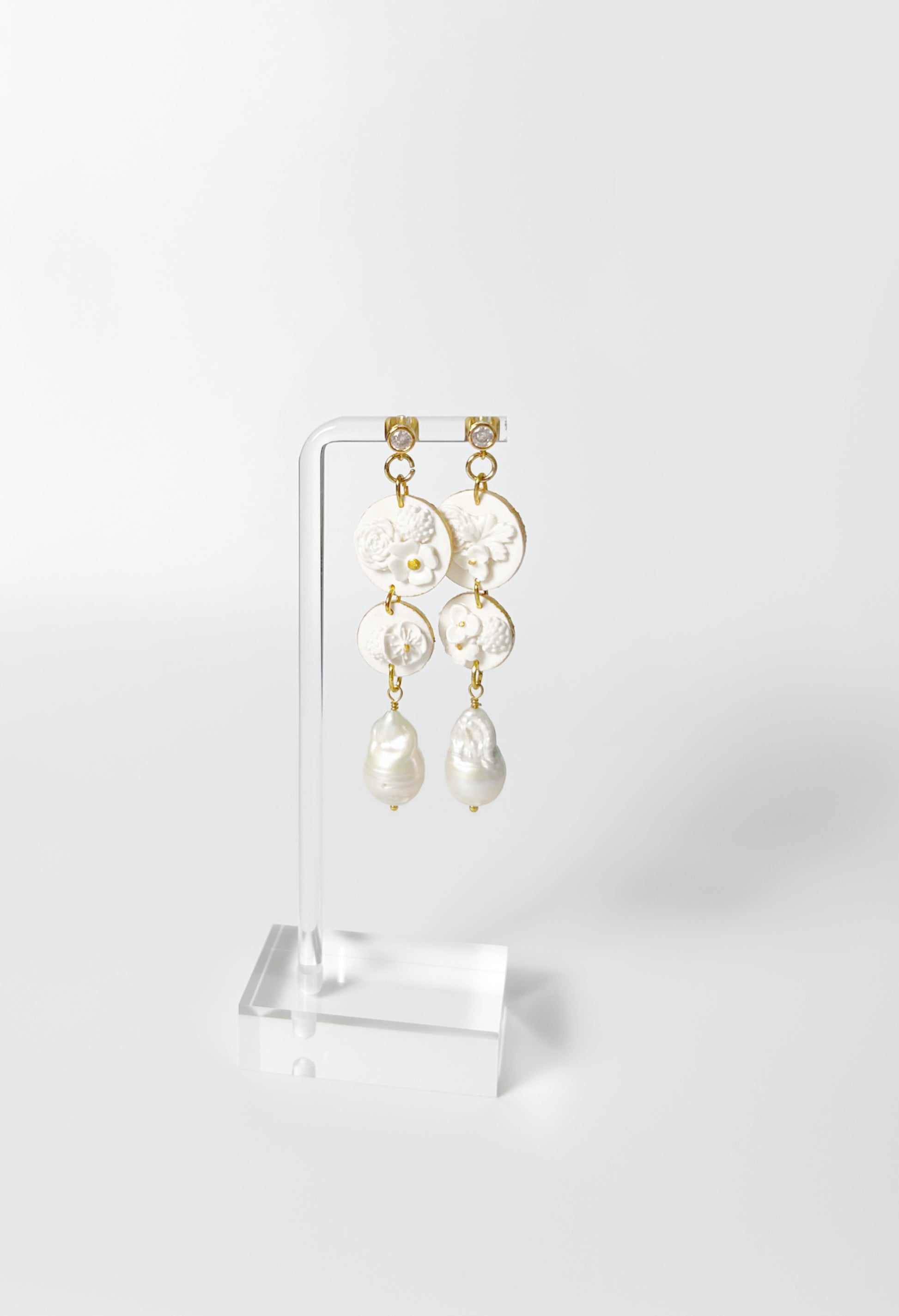 Pair of pearl earrings on a clear stand against a white background