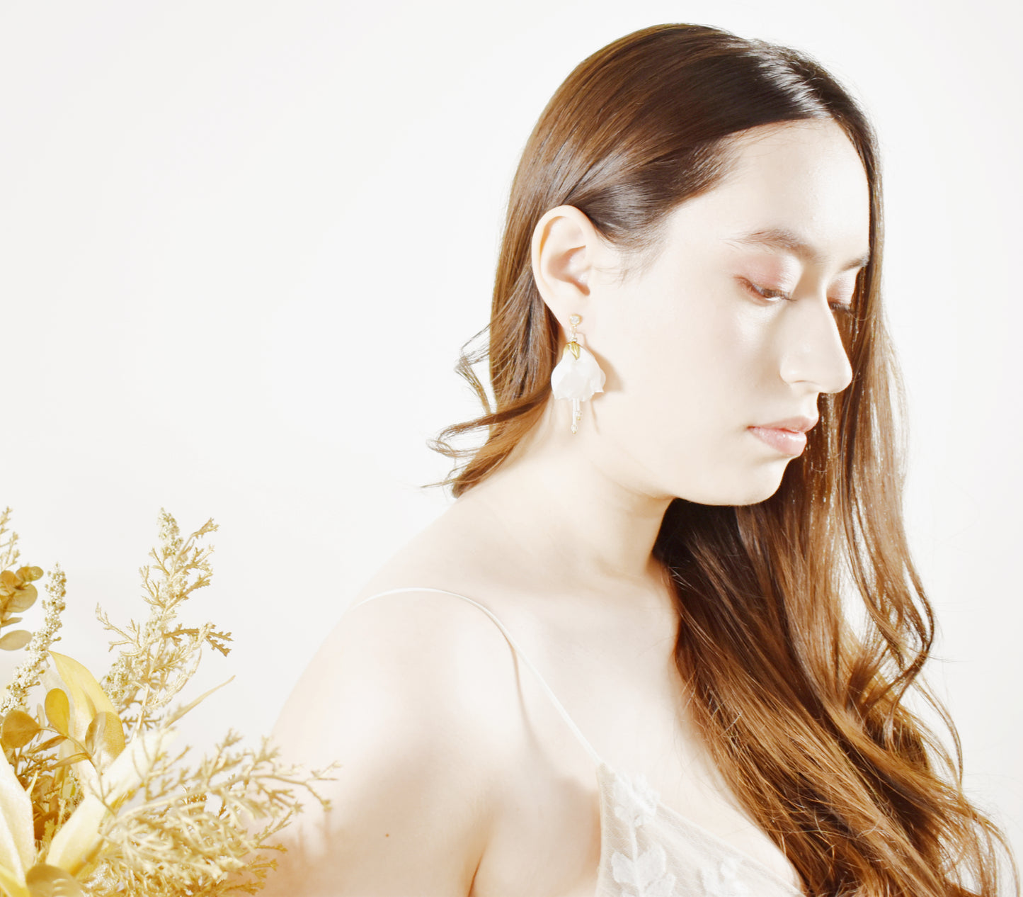 Woman with long brown hair wearing gold earrings against a white background
