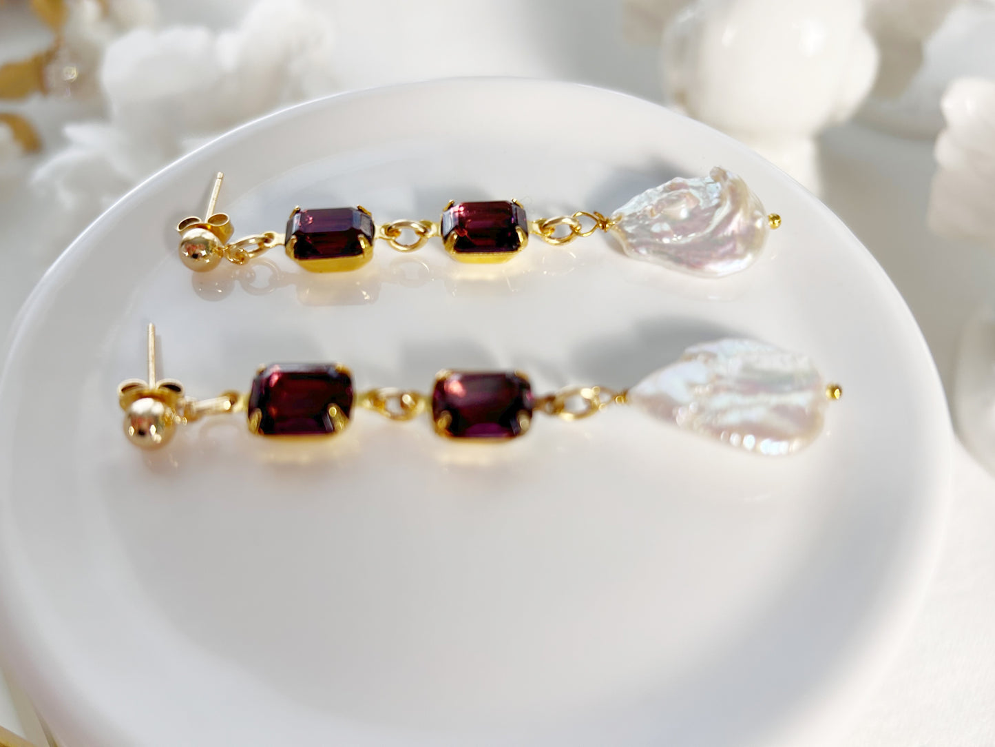 Pair of gold earrings with red and clear gemstones on a white surface.
