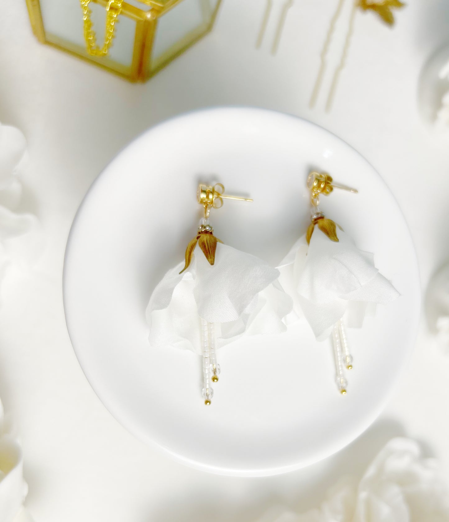 Gold earrings on a white dish with a decorative background