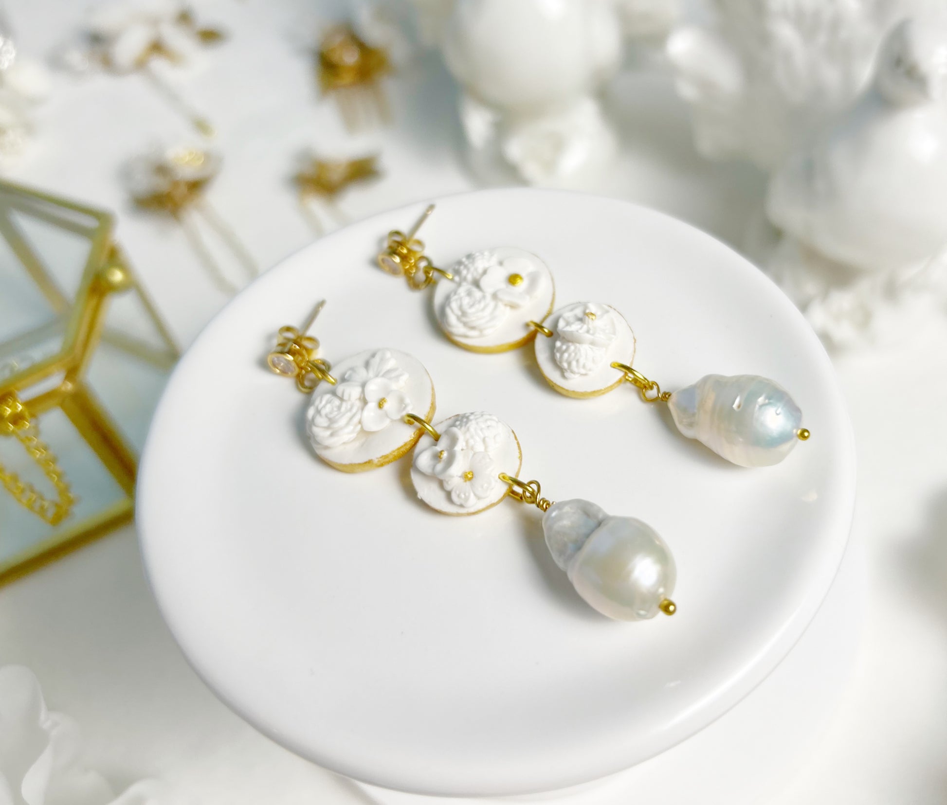 Pair of earrings with floral designs and pearls on a white surface