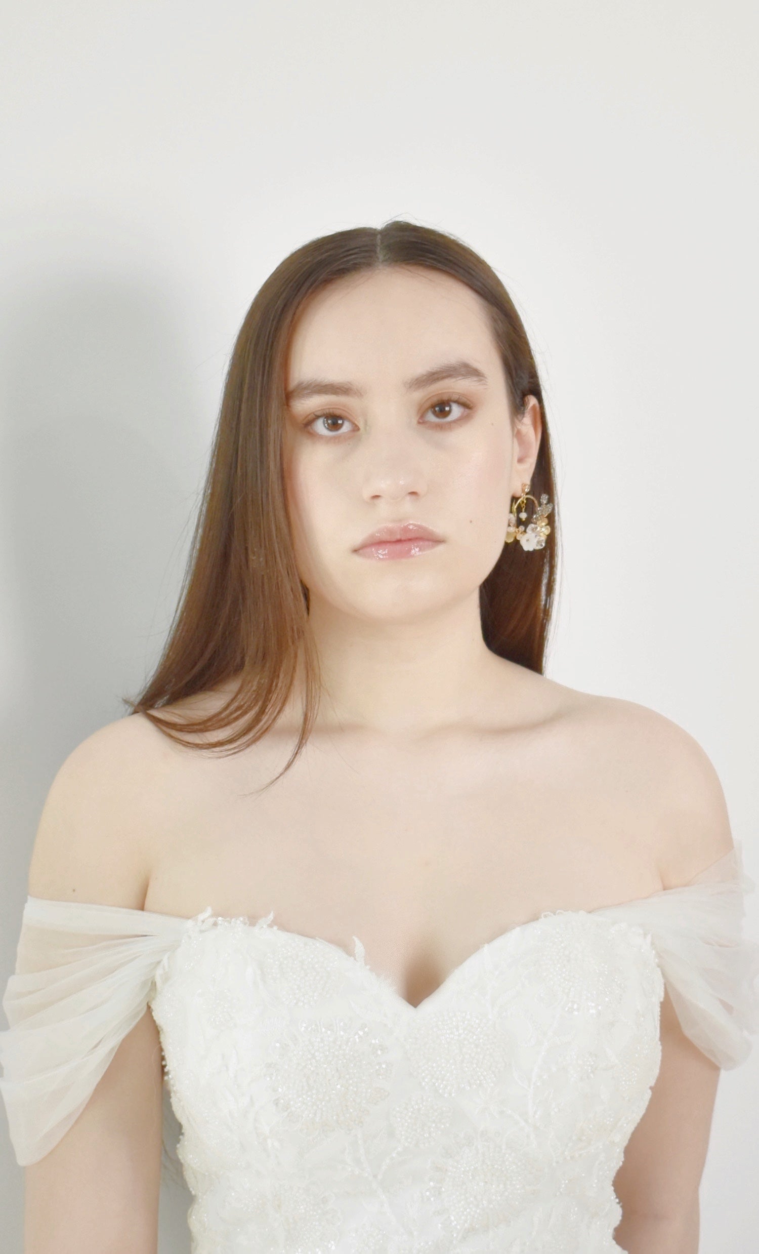 Woman wearing a white off-shoulder dress with sheer sleeves against a plain background