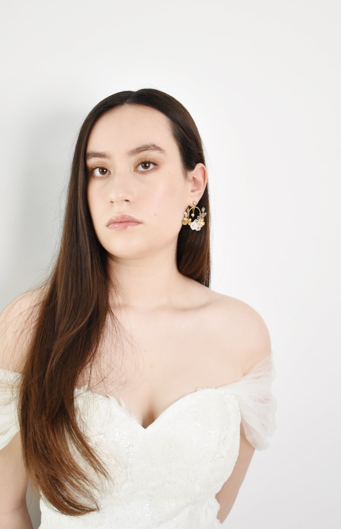 Woman wearing a white off-shoulder top with long dark hair against a plain background