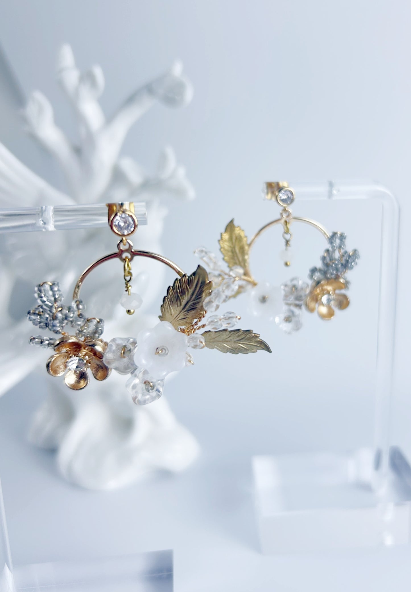 Pair of gold and leaf-themed earrings on a white stand with a light blue background